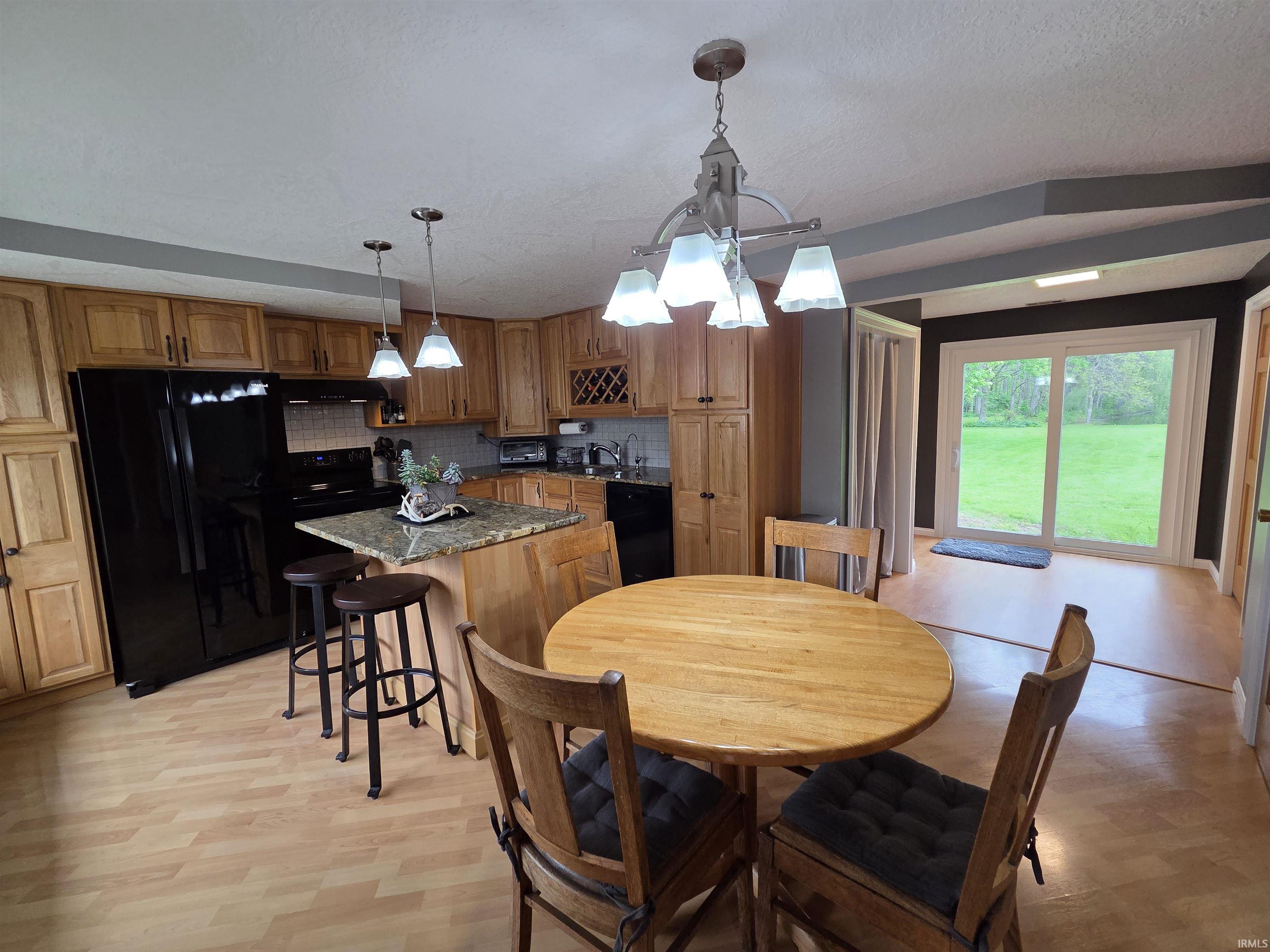 Kitchen featuring light wood-finish cabinetry, black appliances, and an island with a stone-finish countertop