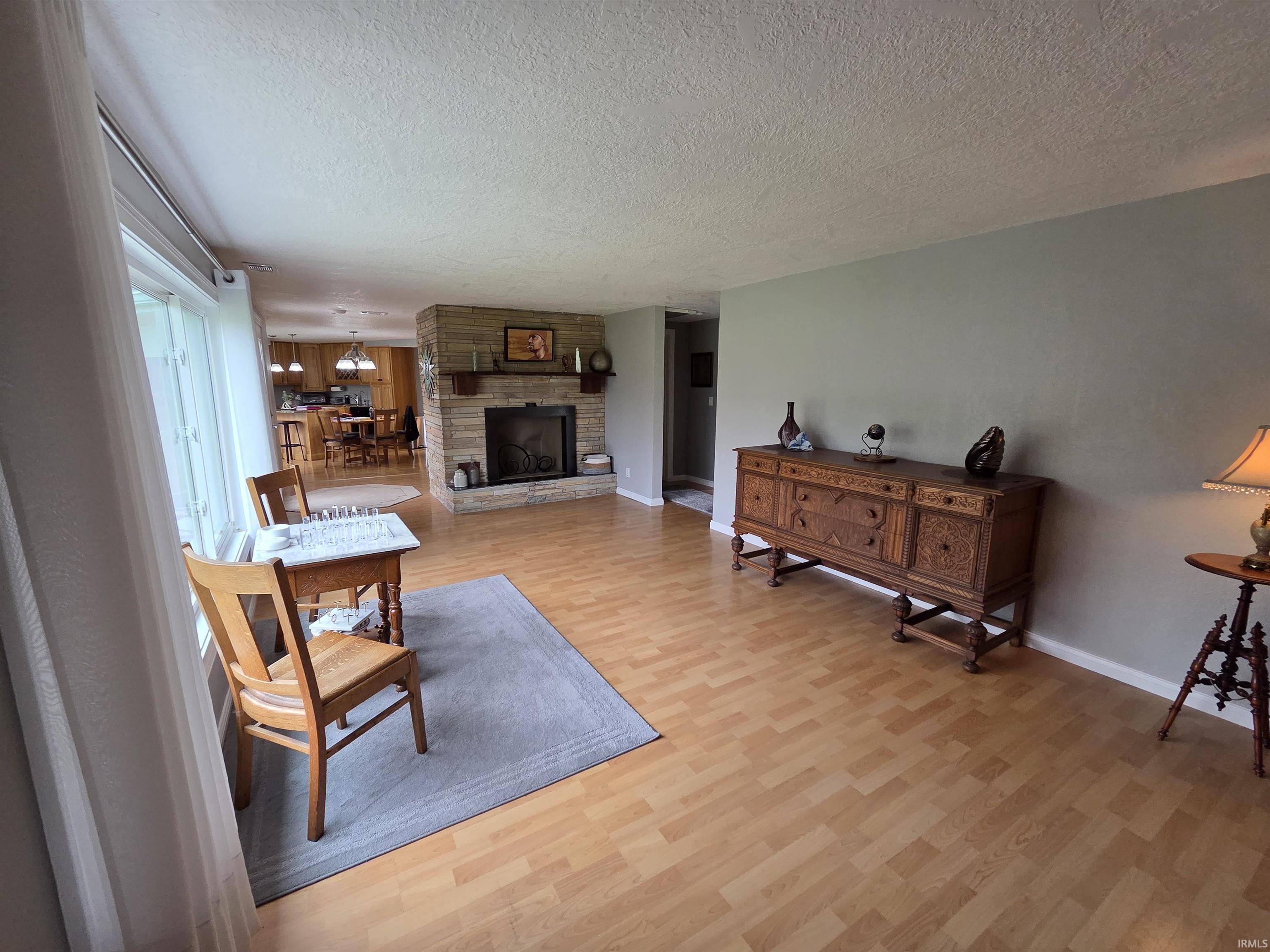 Living area featuring wood-finish flooring, a stone fireplace with a wood mantel, and large windows