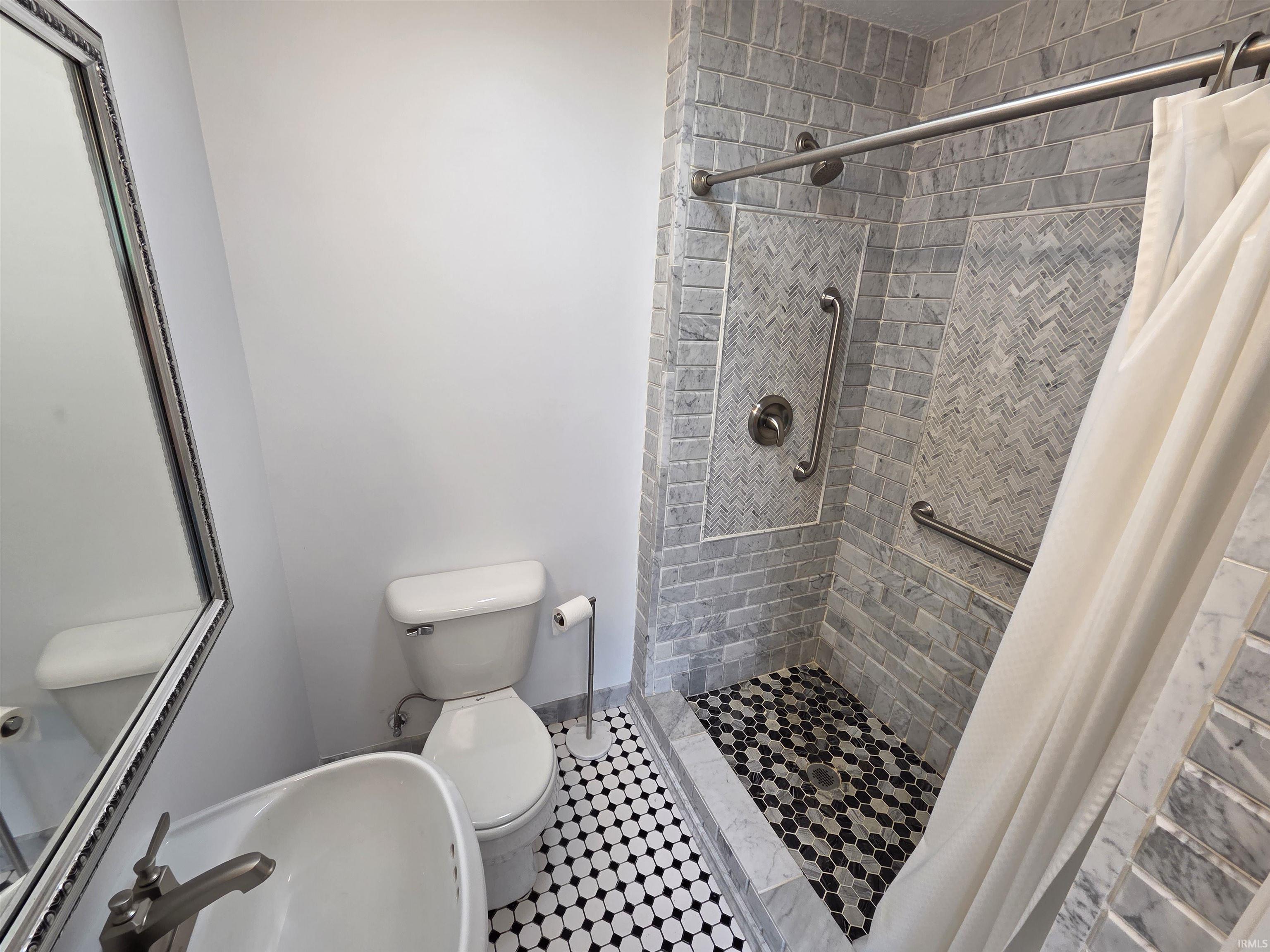 Shower with subway tile walls, herringbone tile accents, and a black and white hex tile floor