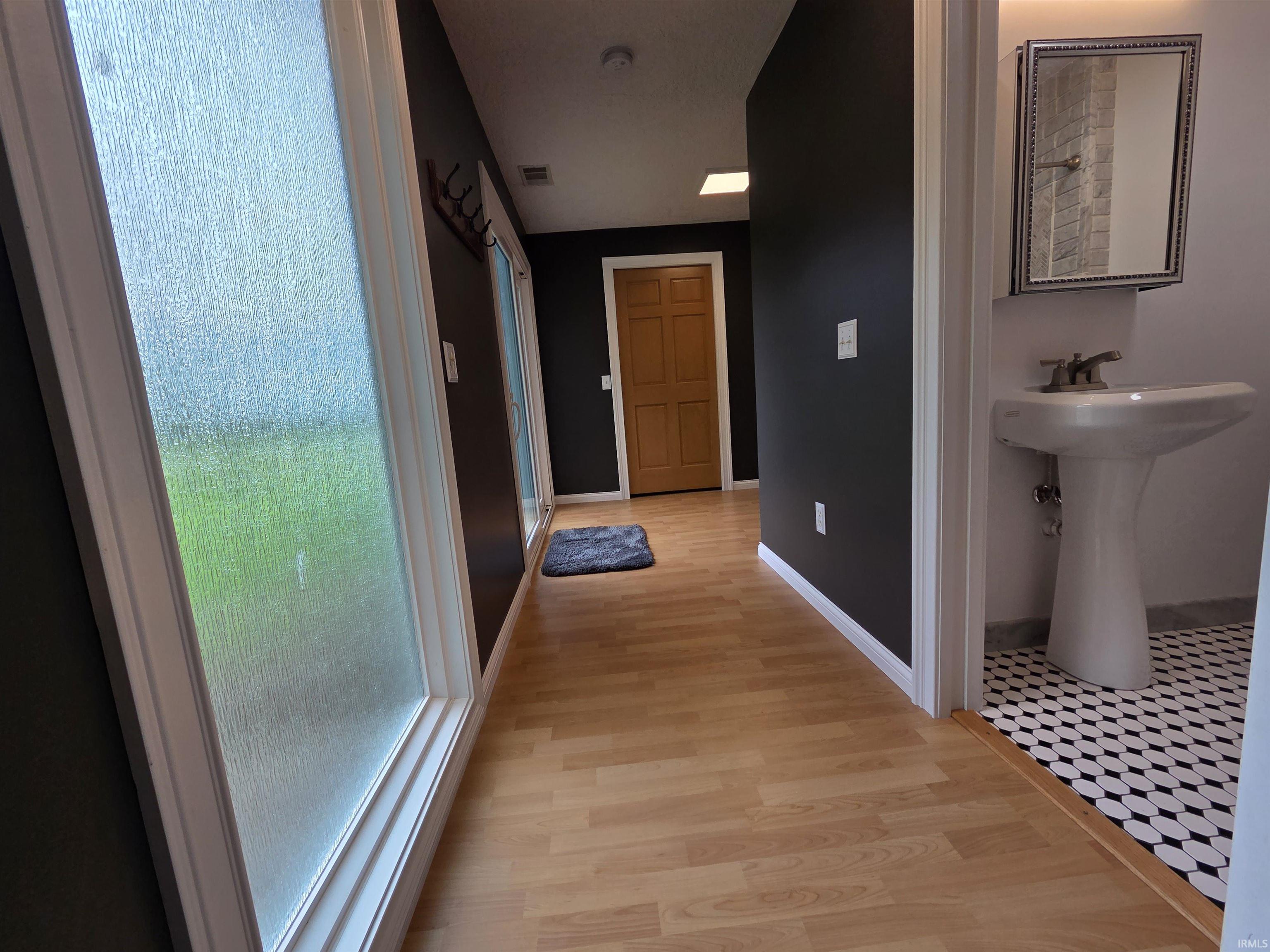 Hallway featuring wood-finish flooring, dark wall paint, and a large window with frosted glass