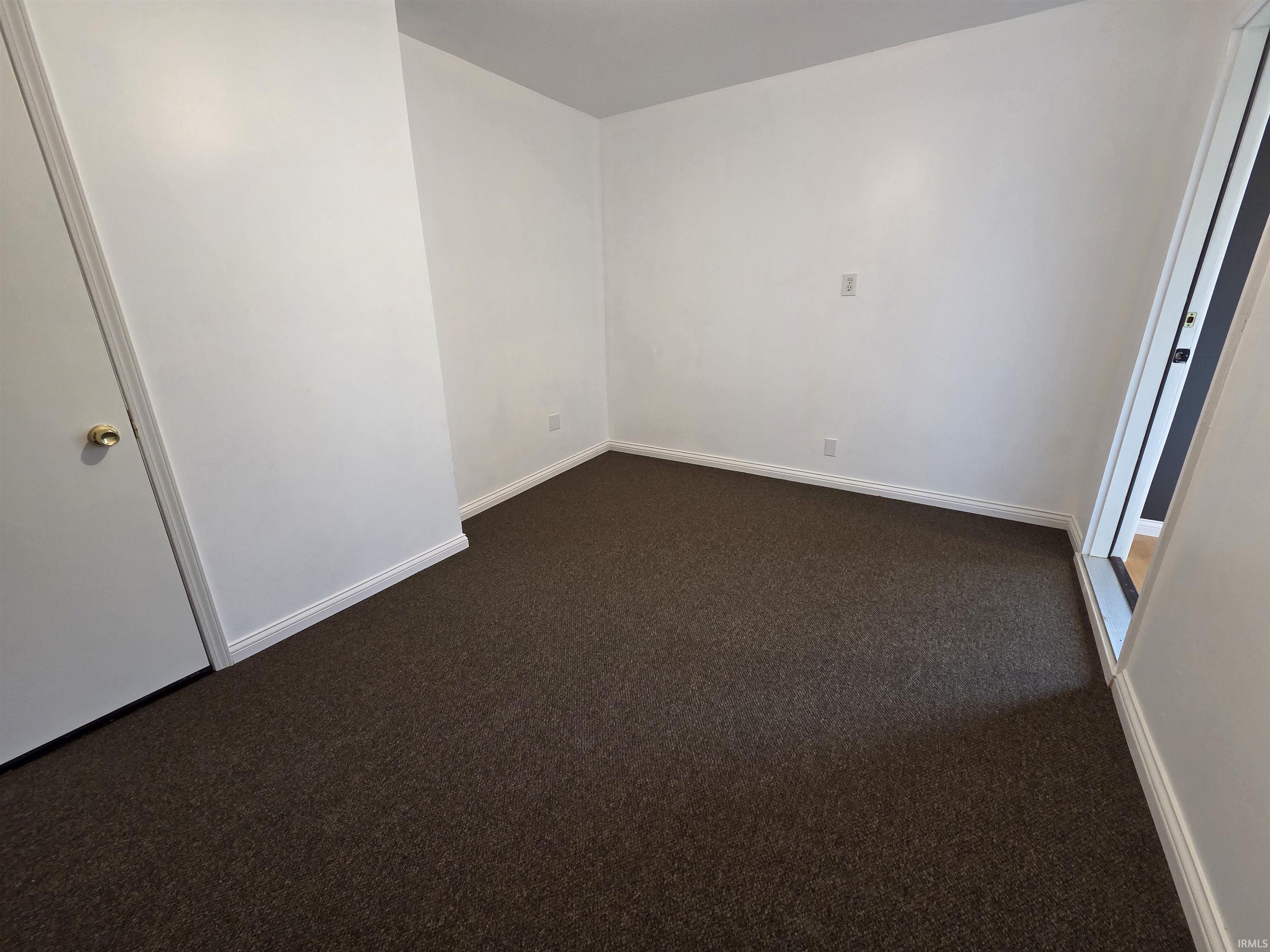 Interior room featuring white walls, dark brown textured carpeting, and white baseboards
