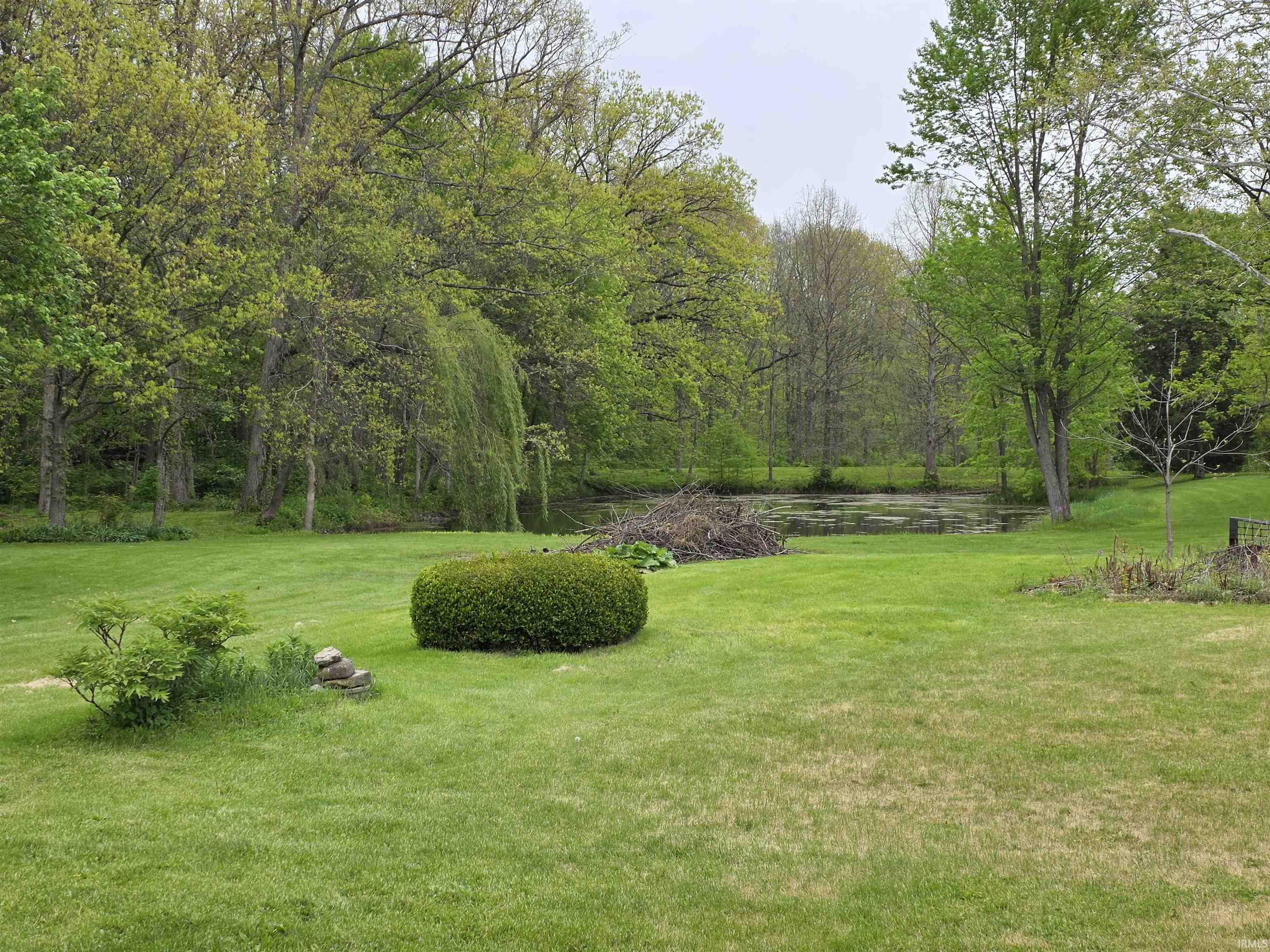 Expansive green lawn with a natural pond border, surrounded by mature deciduous trees