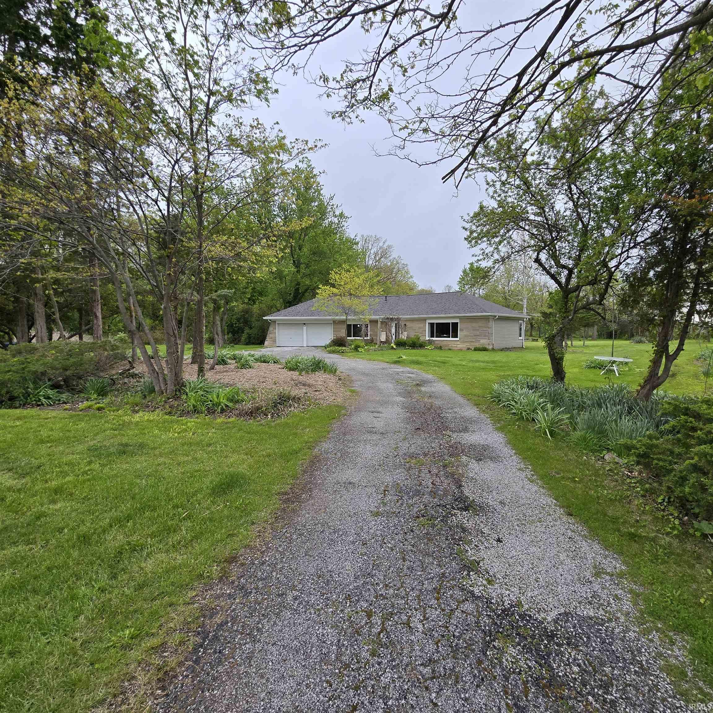 Ranch-style residence featuring a stone-finish exterior, white garage doors, and a dark shingle roof