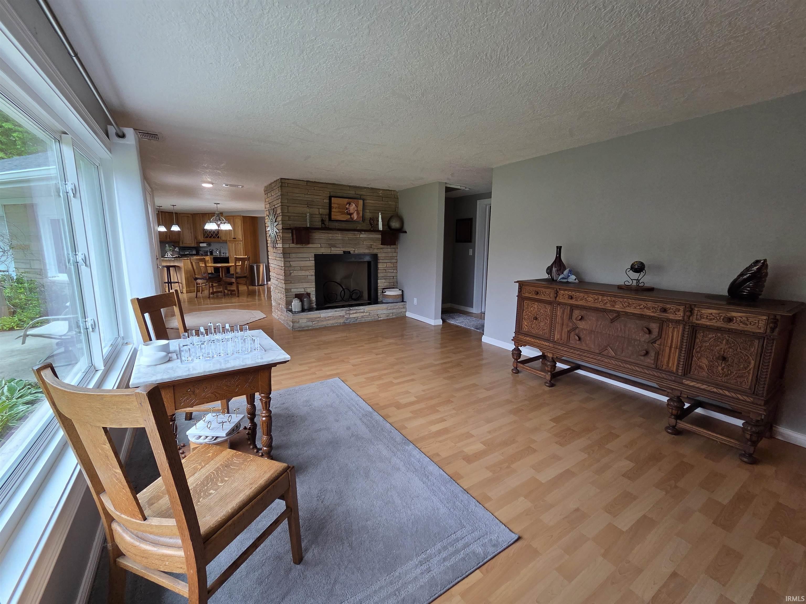 Spacious interior featuring wood-finish flooring, a stacked stone fireplace with a wood mantle, and a large window overlooking exterior landscaping