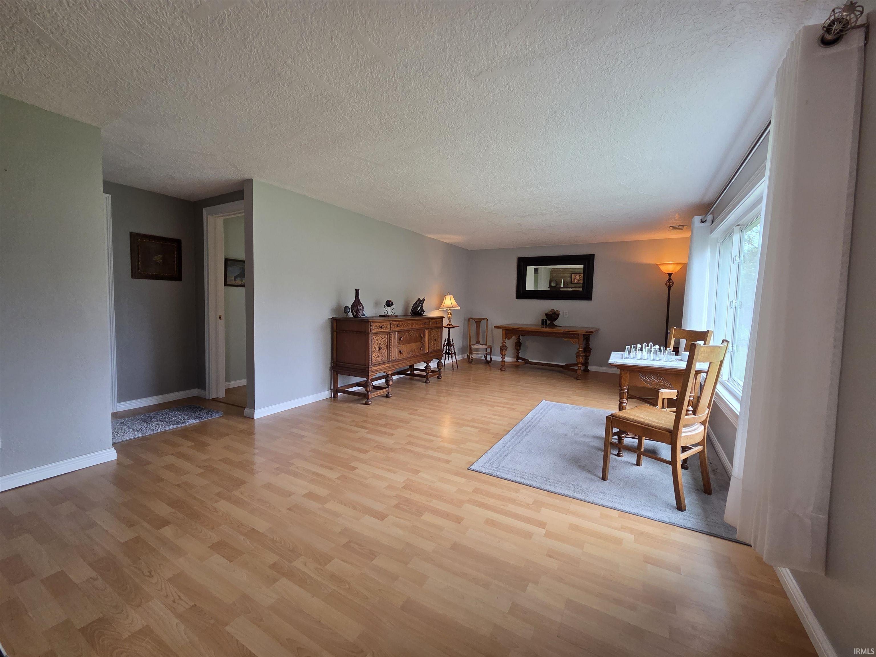 Expansive room featuring light wood-finish flooring, neutral gray wall paint, and white baseboards