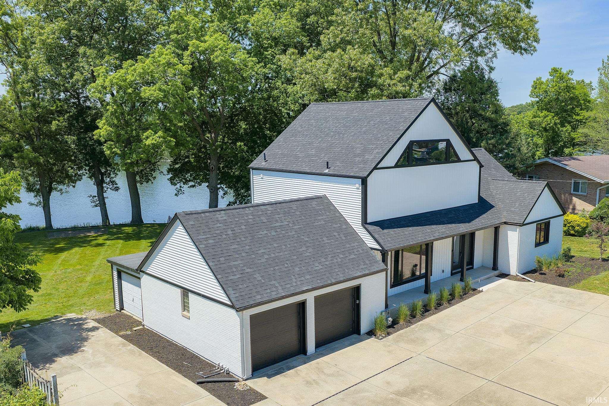 Contemporary architectural design featuring white siding with black trim, a dark shingle roof, and a prominent triangular window