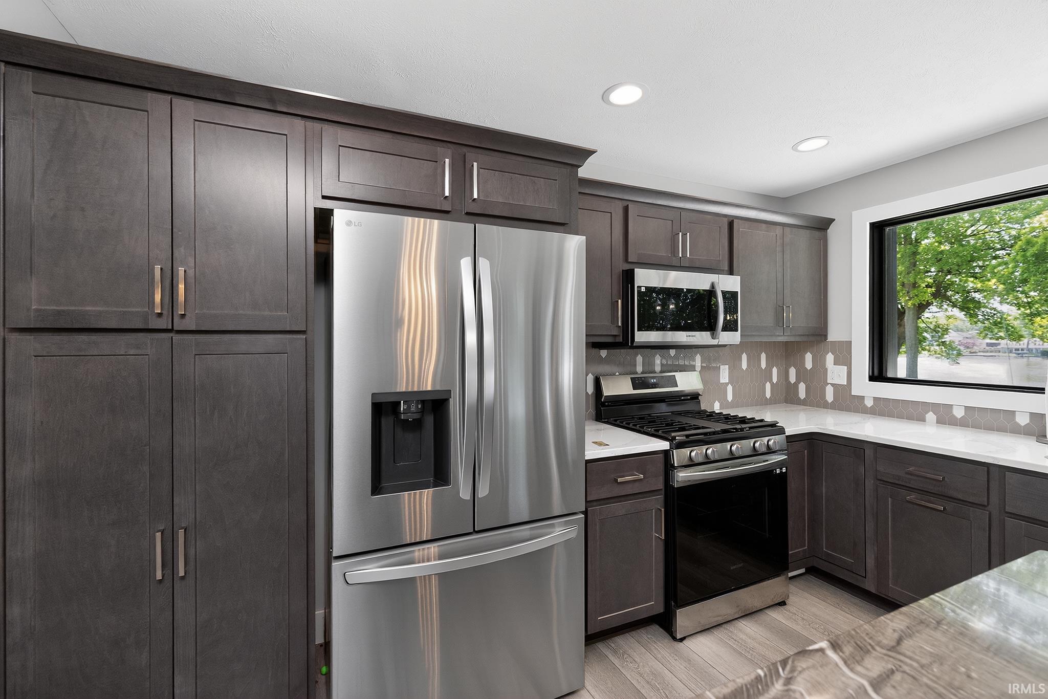 Modern kitchen featuring dark wood-finish cabinetry, stainless steel appliances, recessed lighting, white countertops, and a unique geometric backsplash