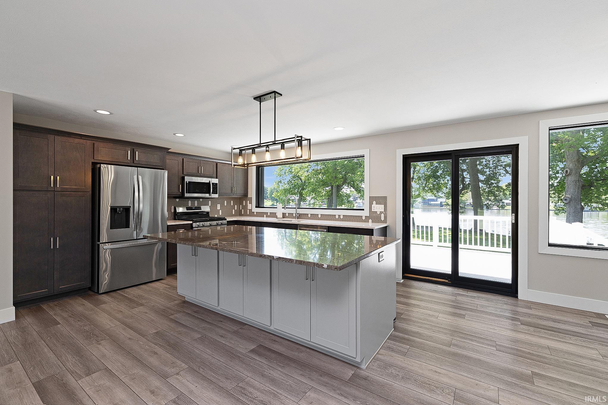 Kitchen featuring a central island with a stone countertop, dark wood-finish cabinetry, stainless steel appliances, and wood-finish flooring