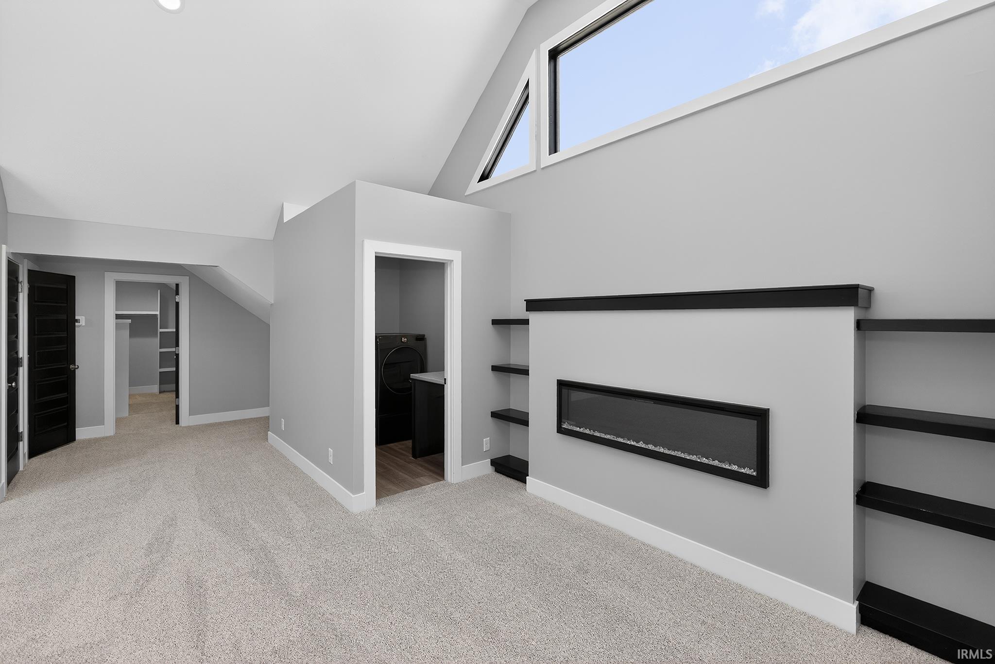 Spacious loft area featuring an elongated linear fireplace, built-in shelving, vaulted ceilings, and a high transom window