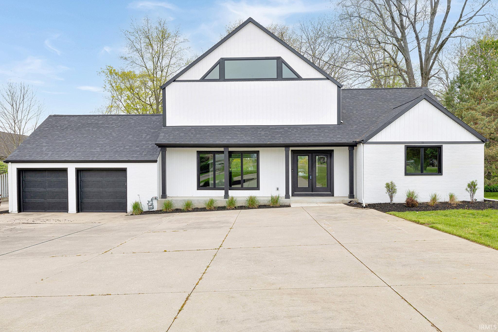 Modern farmhouse exterior featuring contrasting black trim, dual garage doors, a concrete driveway, a prominent gable, and dark-framed windows
