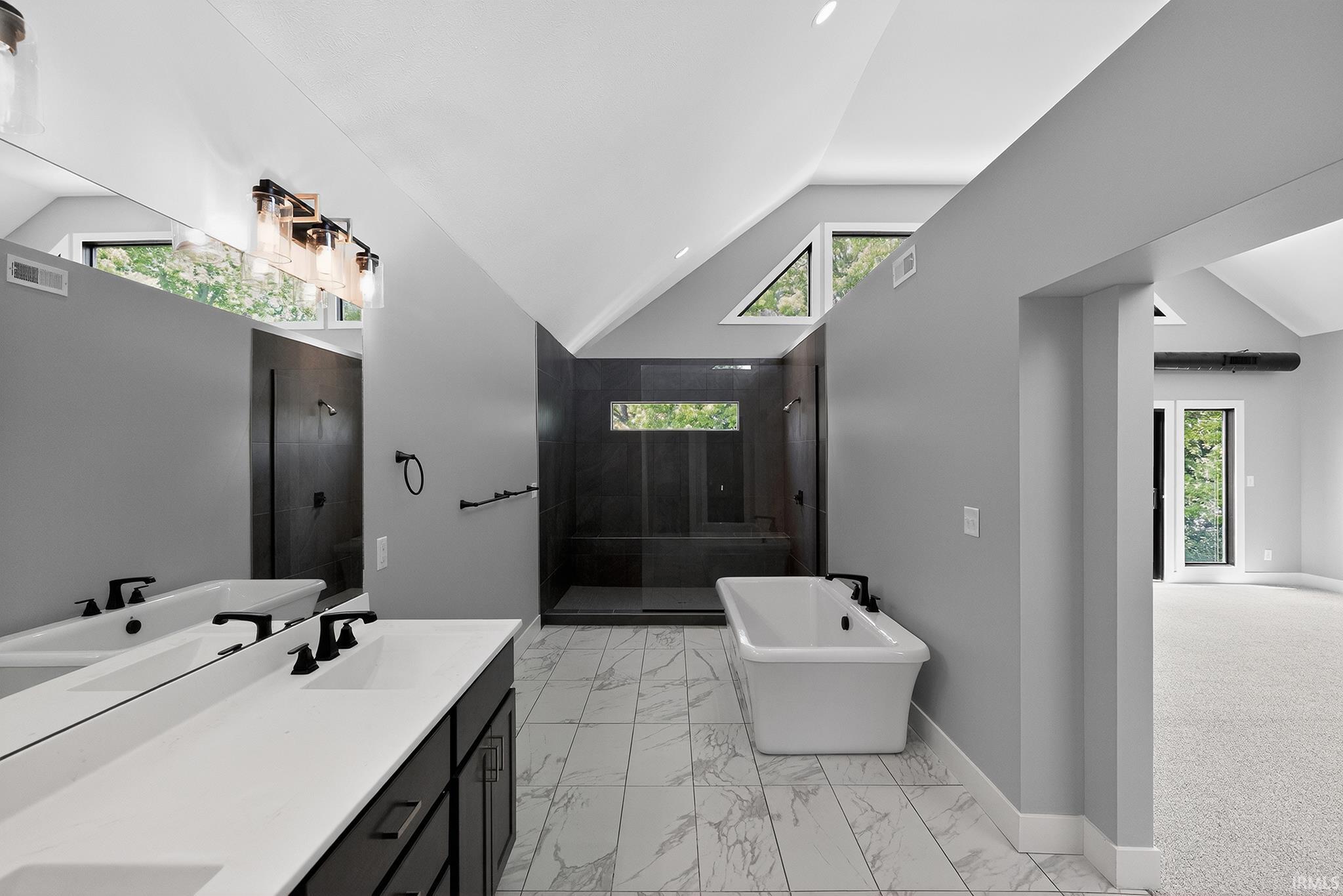 Spacious bath featuring a freestanding tub, dual vanity with undermount sinks, and a walk-in shower with dark tile