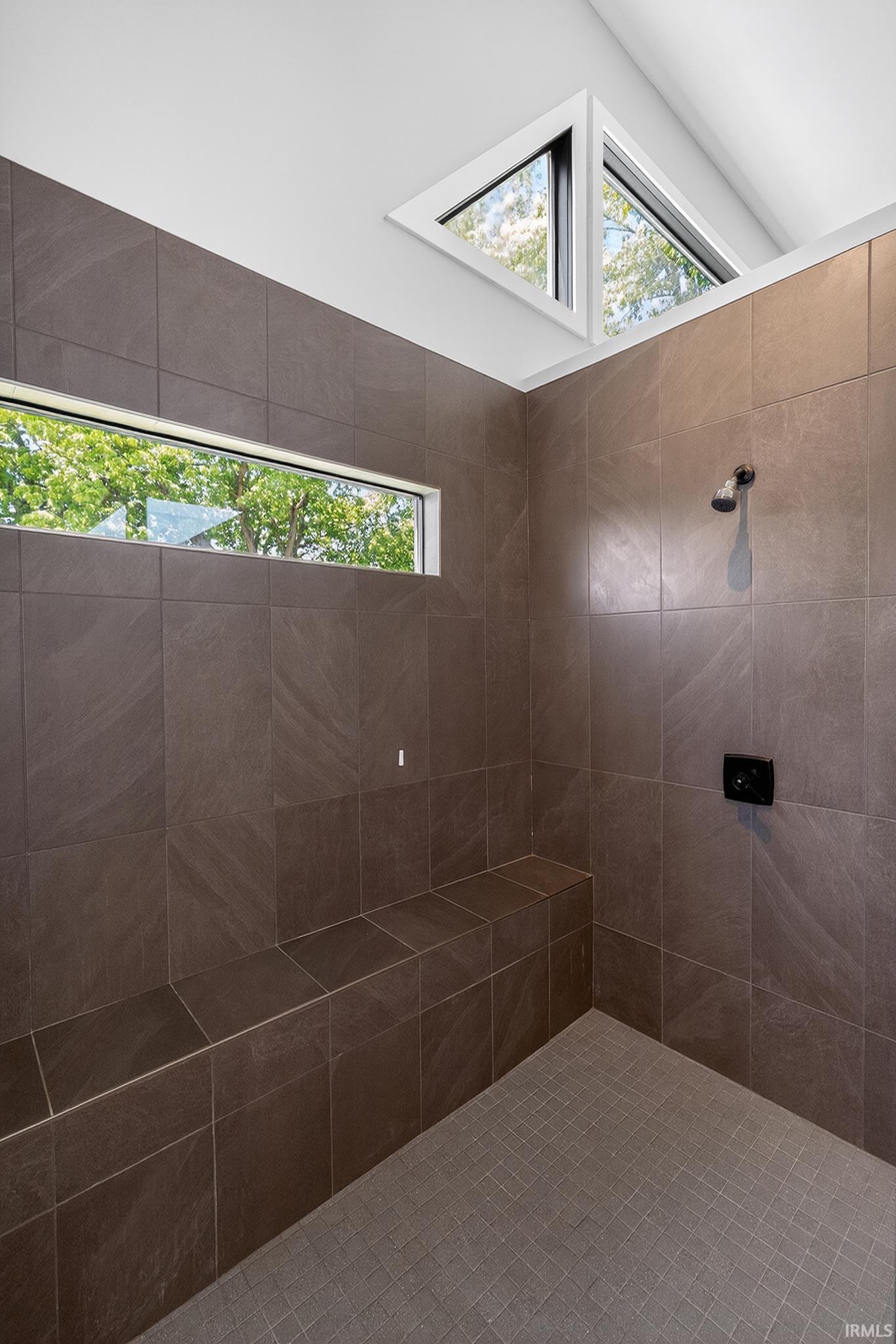 Spacious shower featuring brown tile walls, a built-in tiled bench, a horizontal window, and triangular transom windows