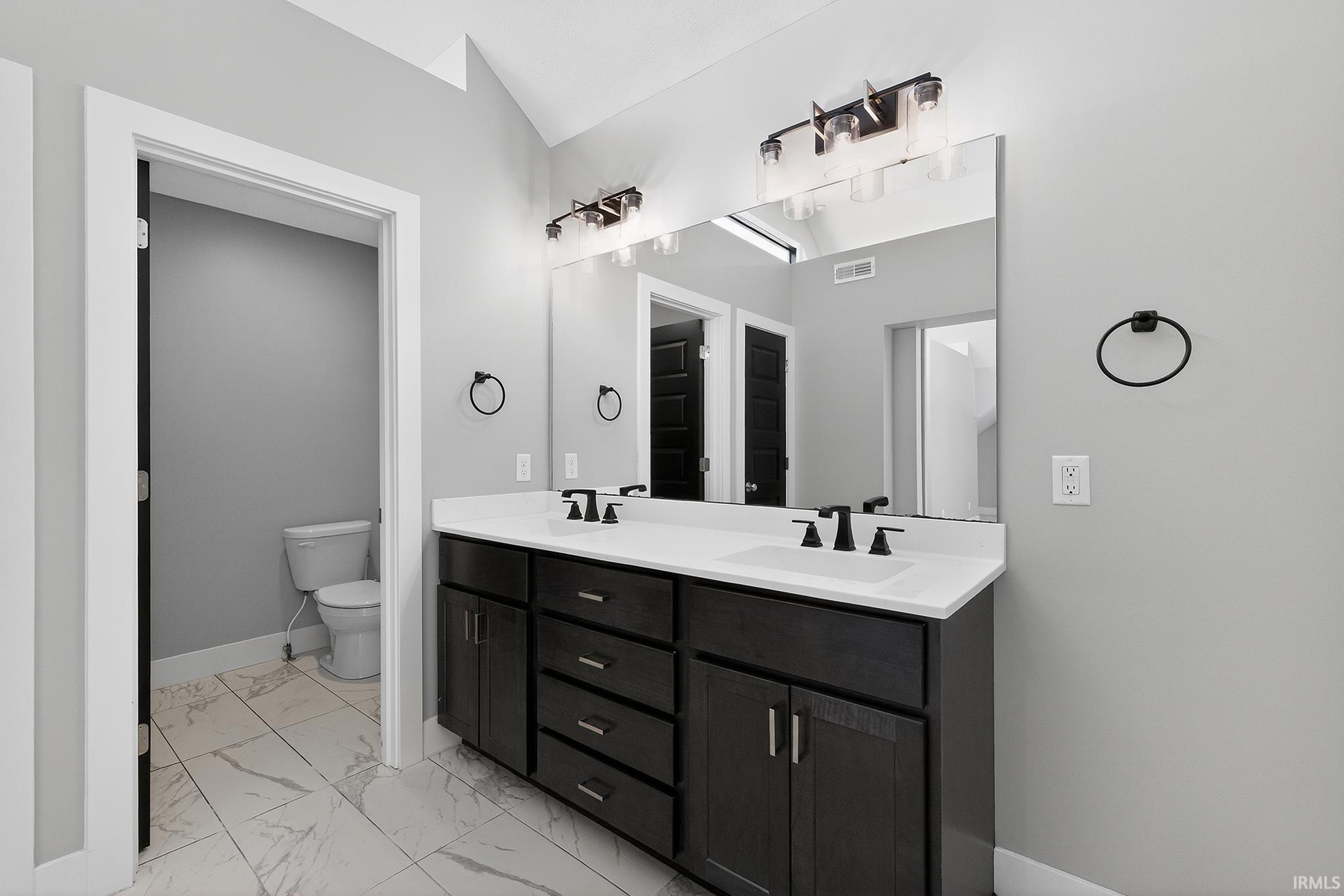 Double vanity featuring dark wood cabinetry, white countertops, and matte black fixtures