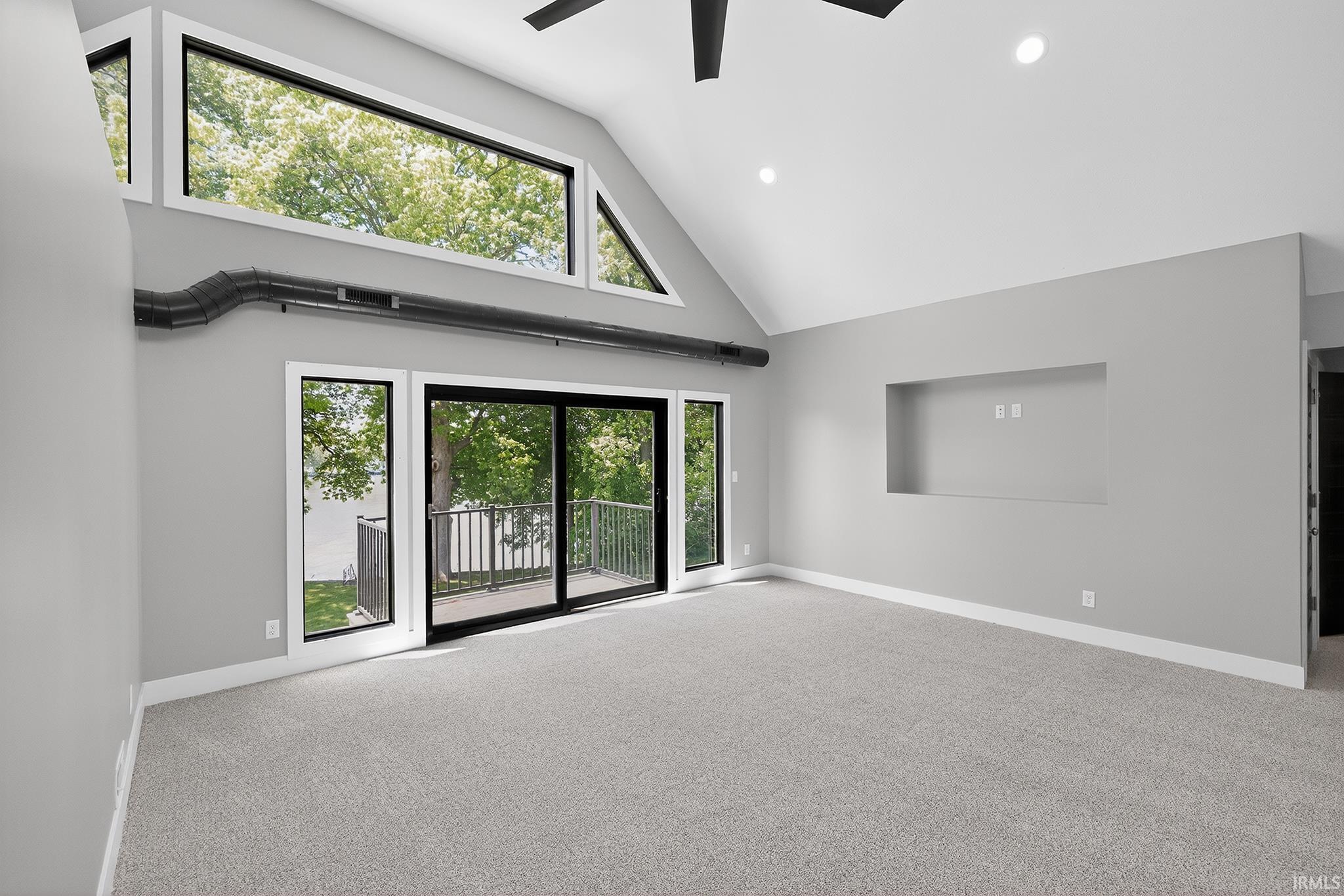 Spacious room with a vaulted ceiling, large upper windows, and direct access to an exterior balcony through sliding glass doors
