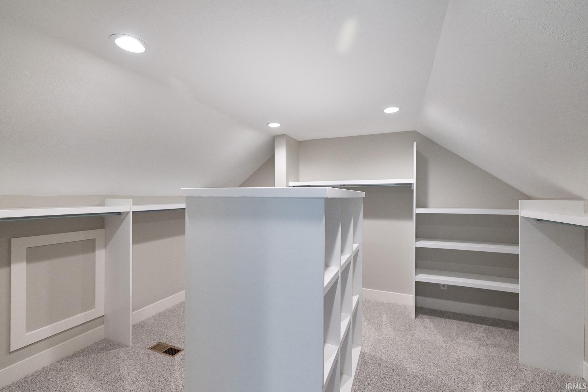 Spacious walk-in closet featuring built-in shelving, a central storage island with integrated compartments, and recessed ceiling lighting
