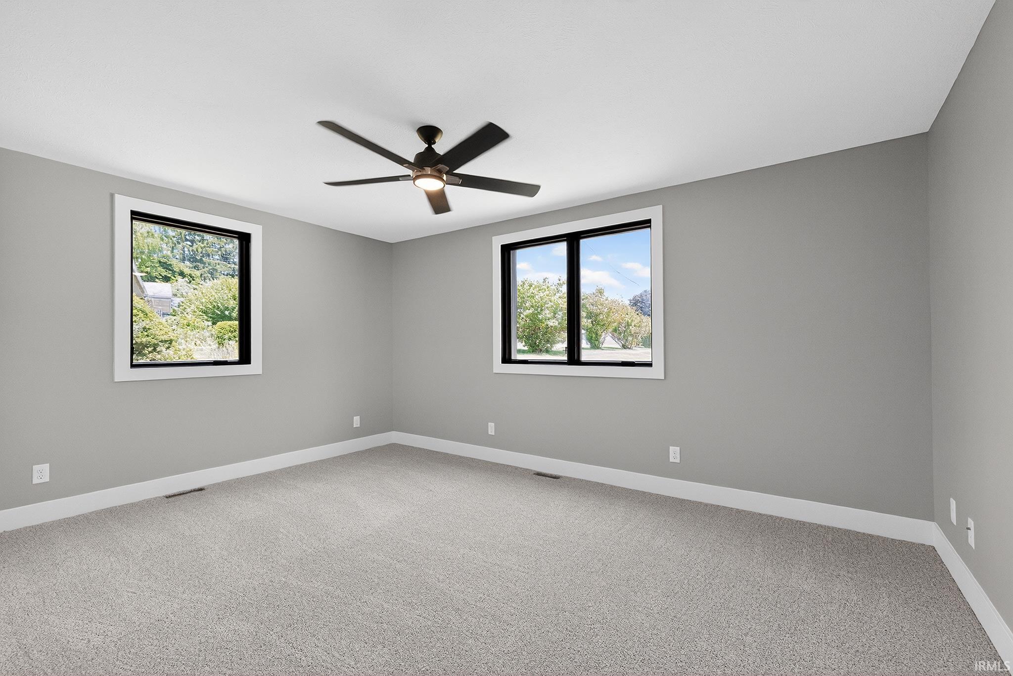 Carpeted room featuring light gray walls, white baseboards, and two windows with black frames