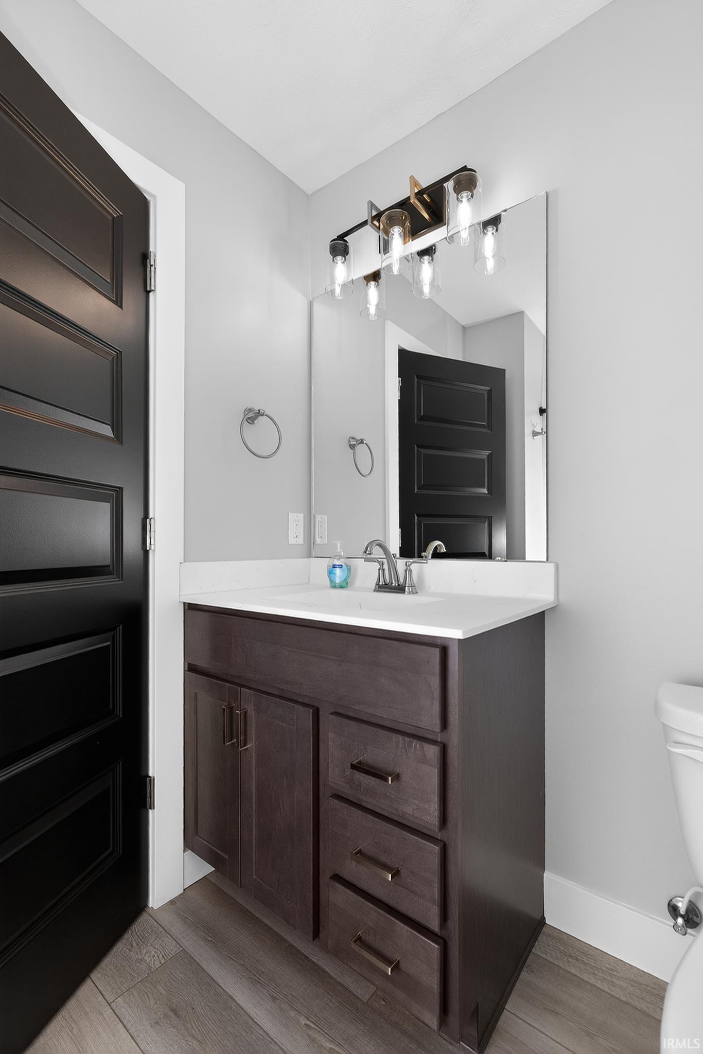 Bathroom vanity featuring a dark wood-finish cabinet with storage drawers, a white countertop, and a contemporary light fixture