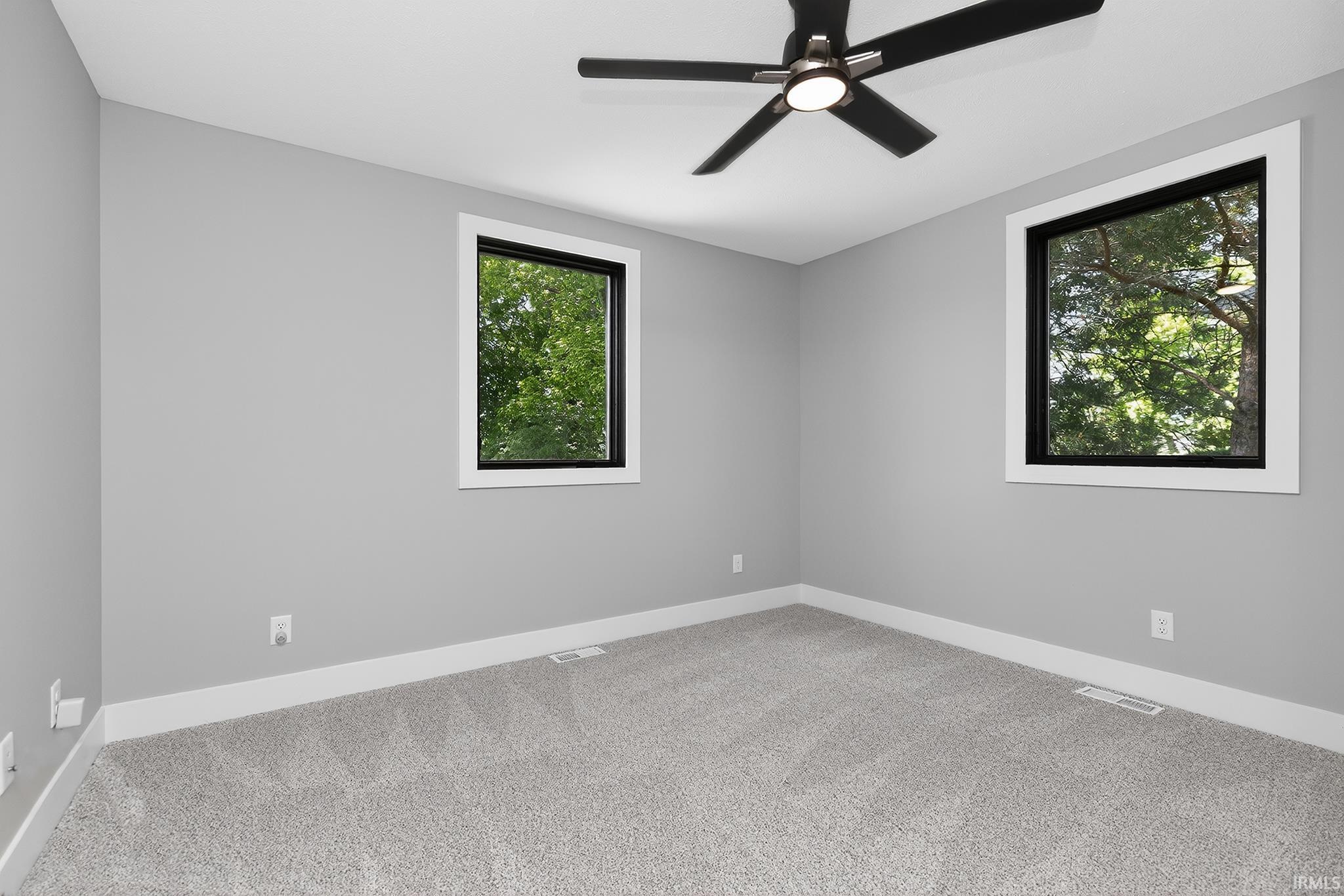 Room with light gray walls, gray carpet, white baseboards, and two windows with white trim and black sashes