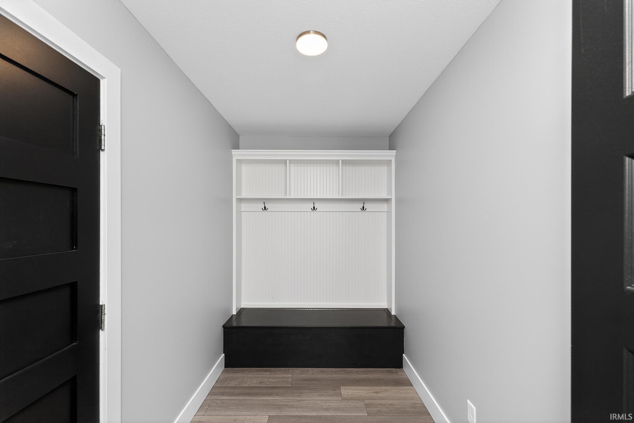 Entryway featuring a built-in white beadboard hall tree with three storage cubbies and three coat hooks, black bench seating, and wood-finish flooring