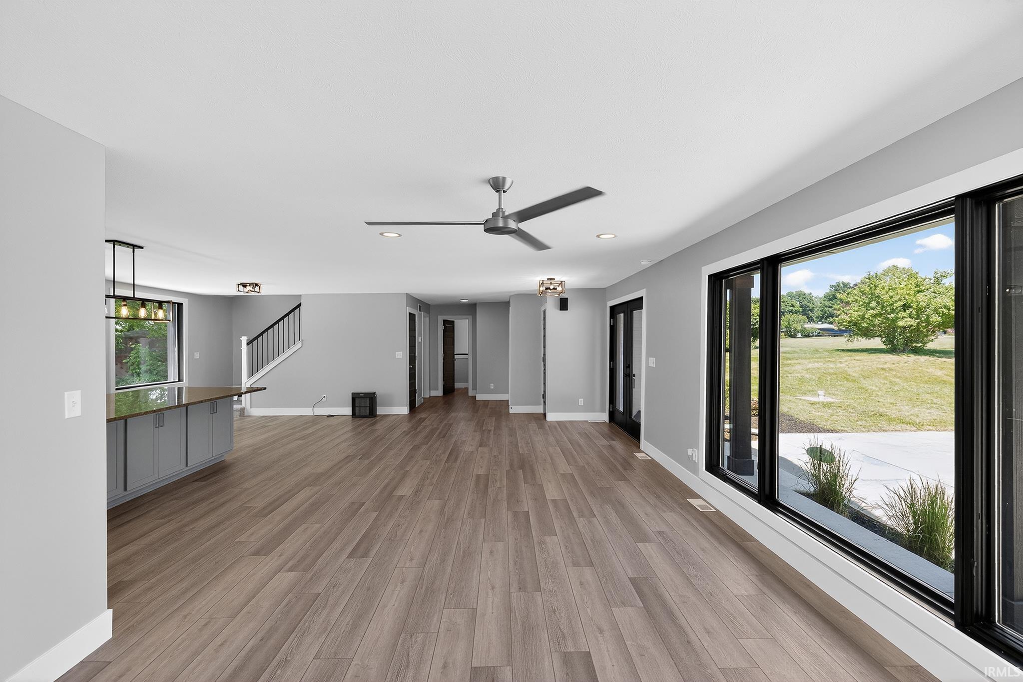 Spacious living area featuring wood-finish flooring, a contemporary ceiling fan, and large black-framed windows