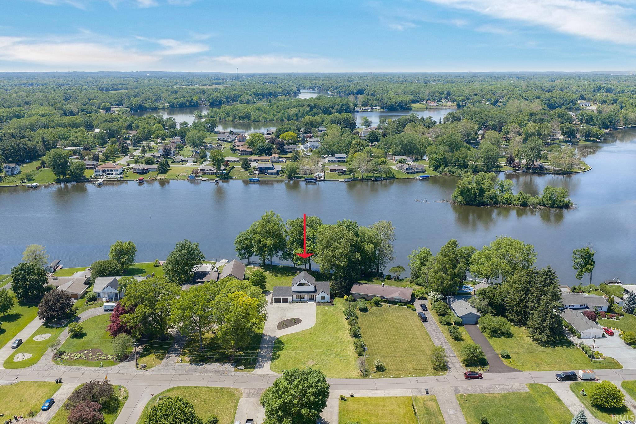 Waterfront property featuring a white exterior with a dark roof, mature trees, a paved driveway, and direct water access