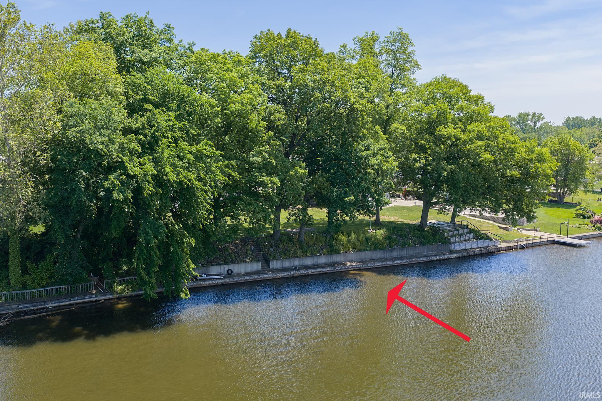 Waterfront property featuring a concrete retaining wall, mature trees, and a private dock structure