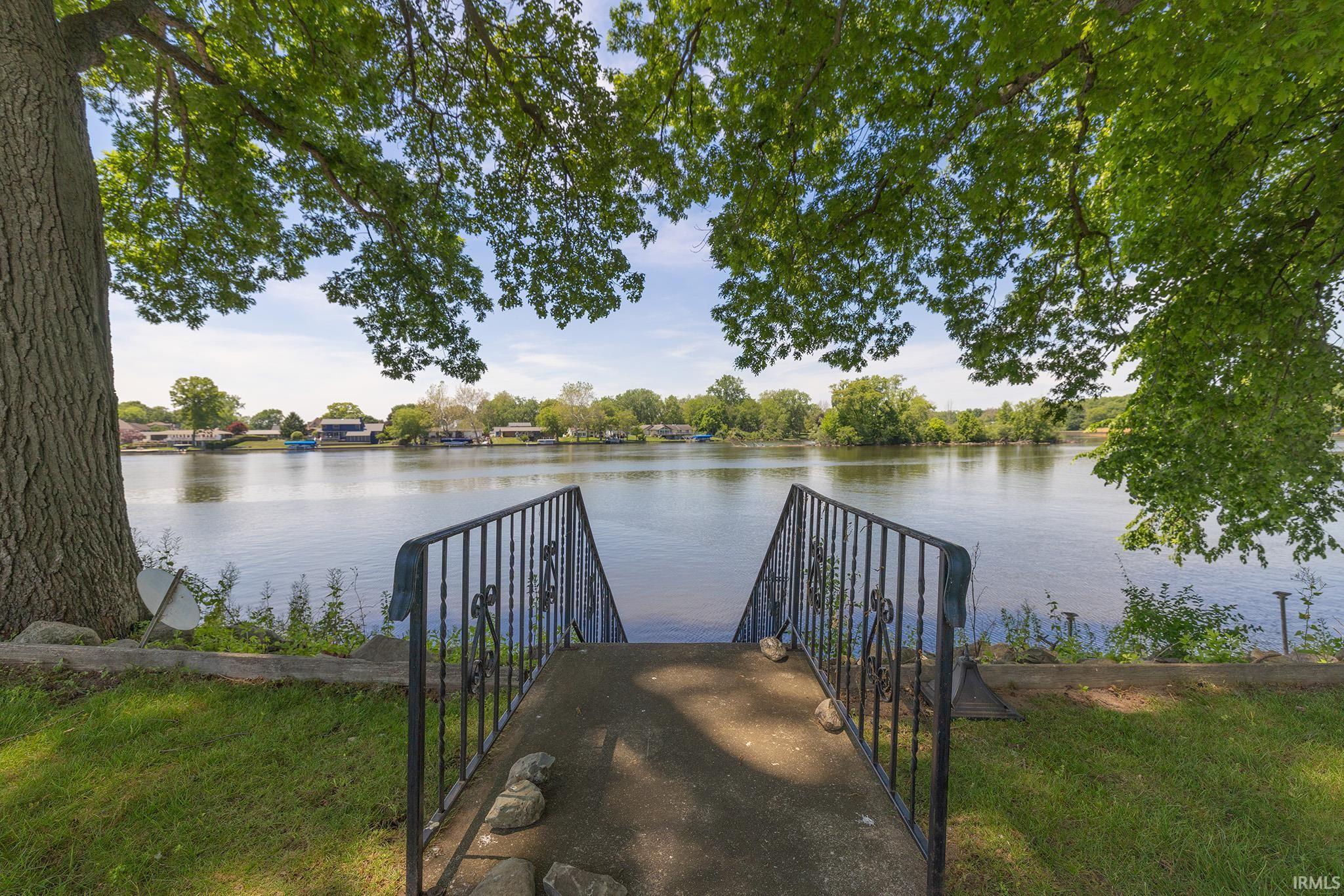 Waterfront property featuring a private concrete stairway with wrought iron railings, mature trees, and a grassy lawn area