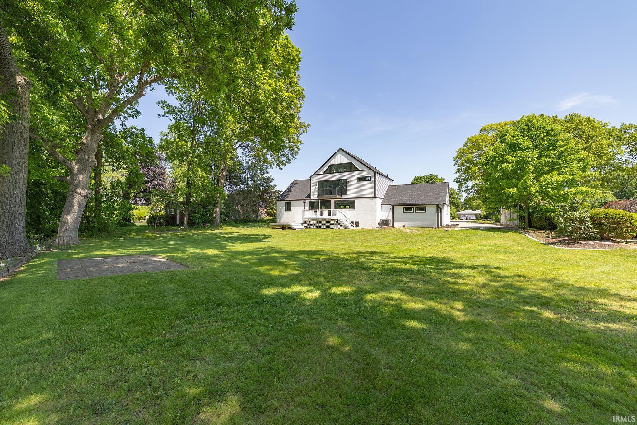 Expansive lawn with mature trees and a modern-style home featuring white siding, black trim, and a multi-level deck