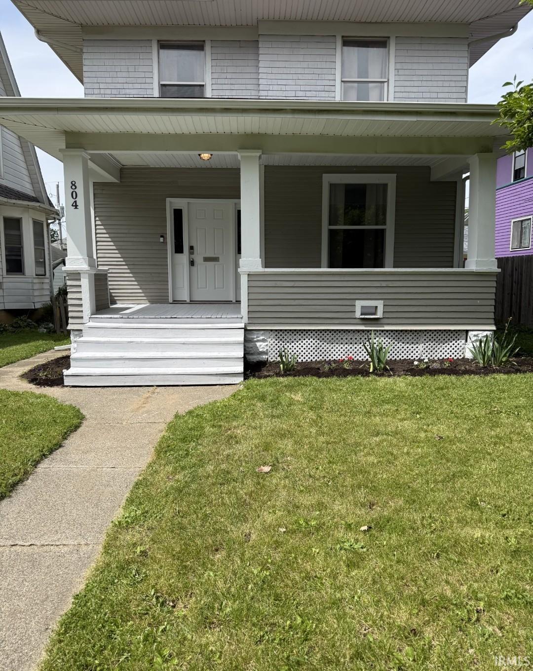 Two-story property featuring a covered front porch with white columns, a white paneled entry door with sidelights, and light gray horizontal siding on the lower level