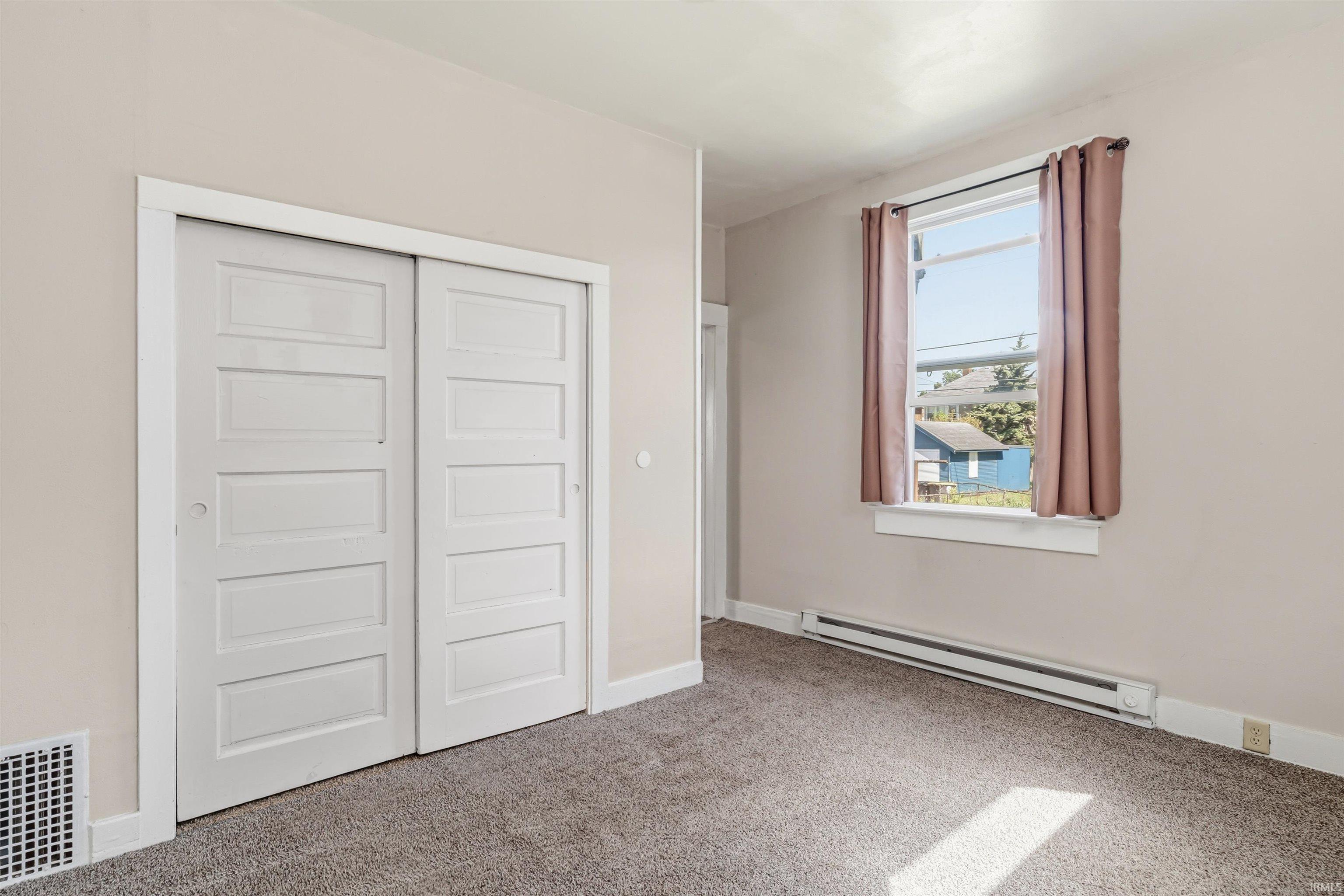 Carpeted room featuring a double-pane window, baseboard heating, sliding panel closet doors, and light-toned wall paint