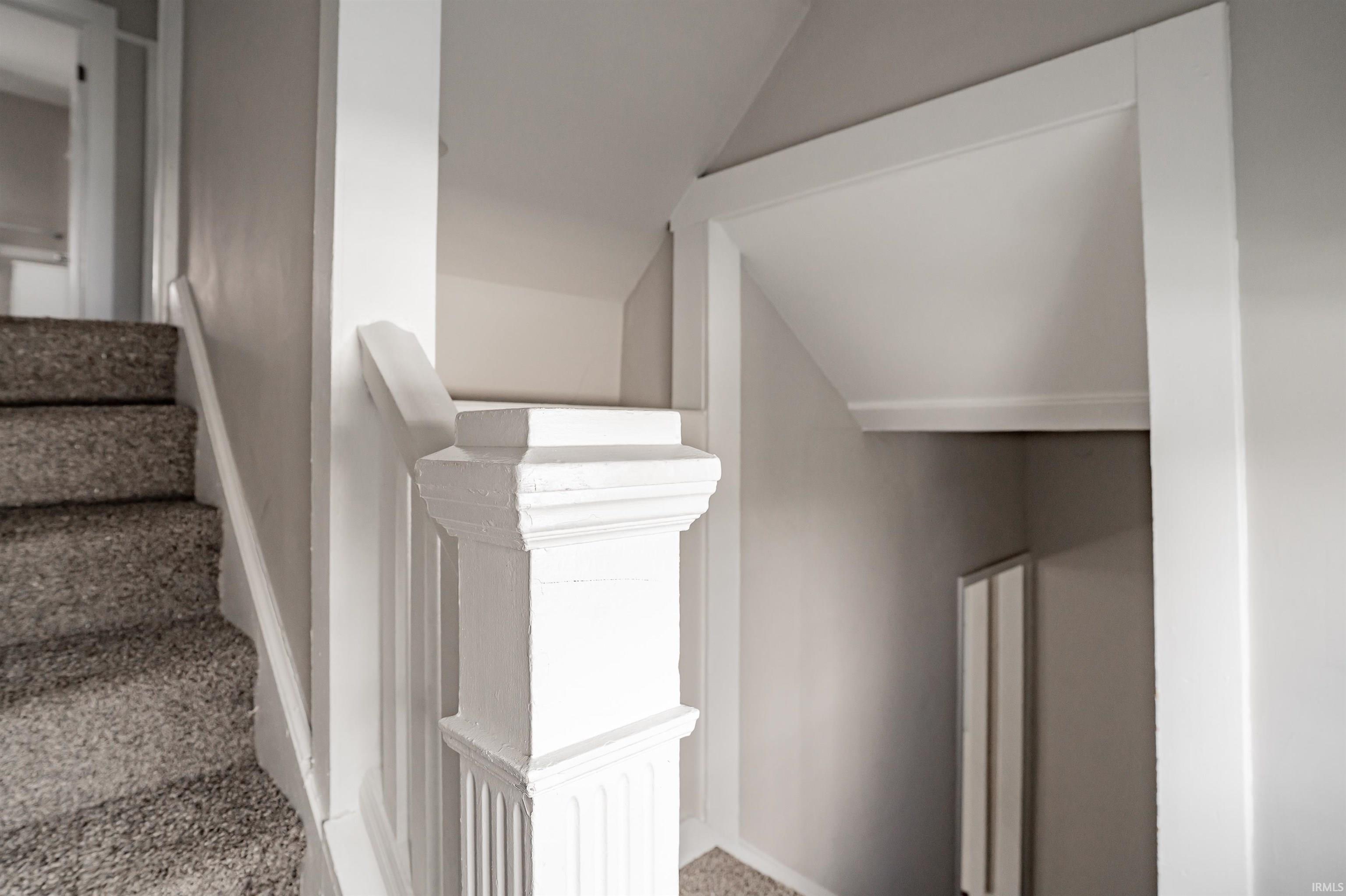 Staircase with carpeted treads, white painted newel post, and matching handrail, framed by a doorway with white trim
