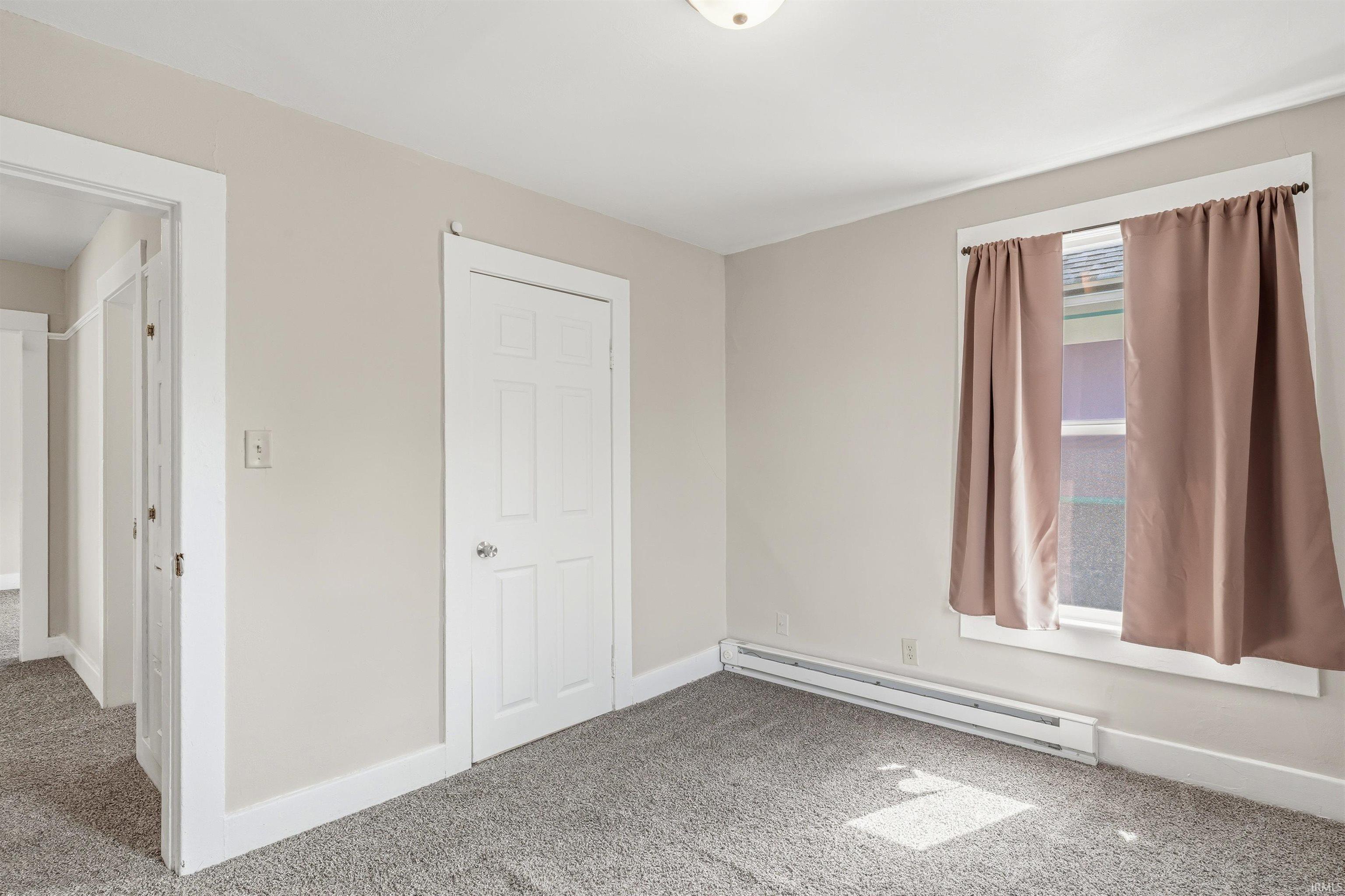 Carpeted room featuring a white paneled door, a window with white trim, and a baseboard heater