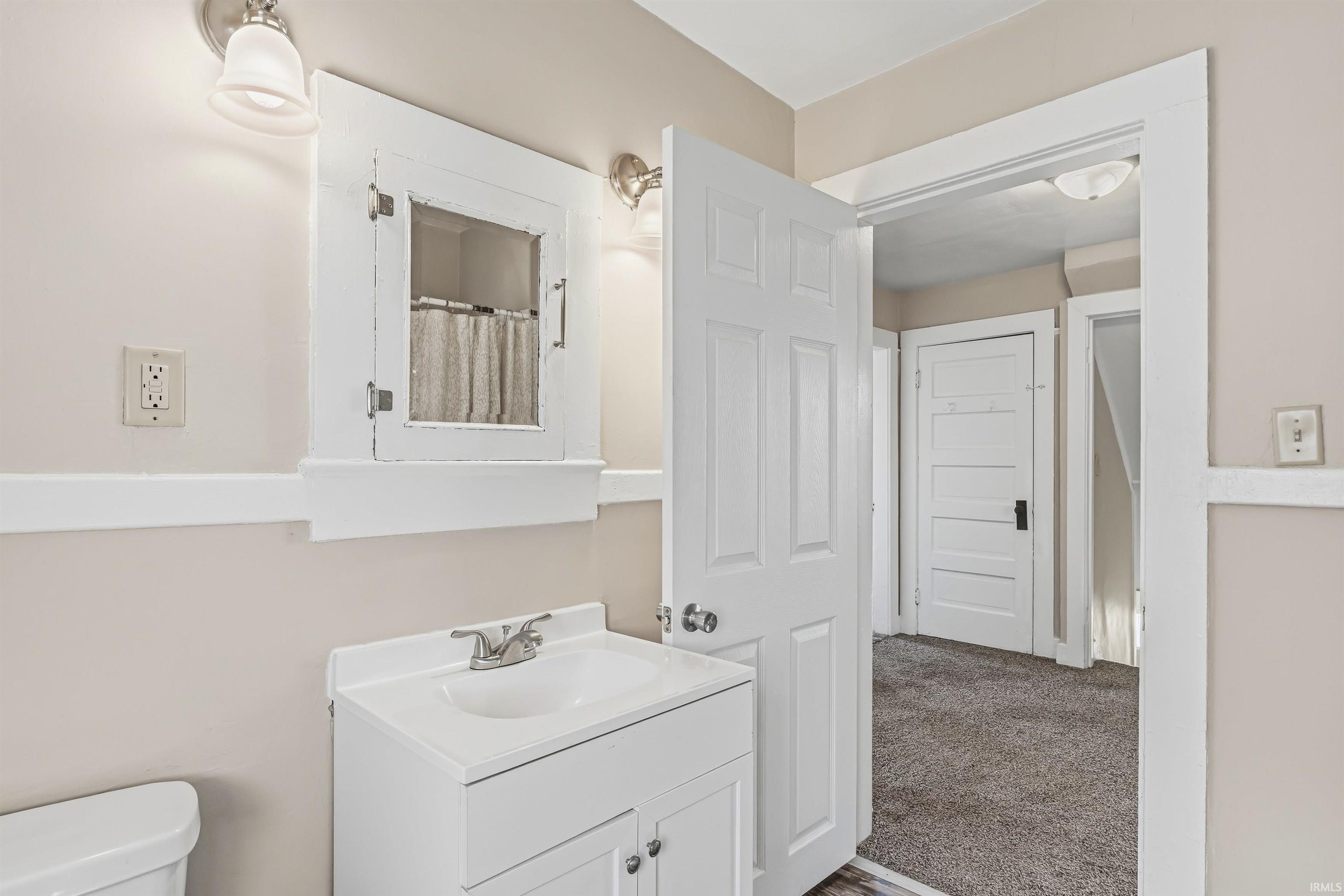 Bathroom featuring a white vanity with integrated sink, chrome faucet, medicine cabinet with mirrored door, and dual wall sconces