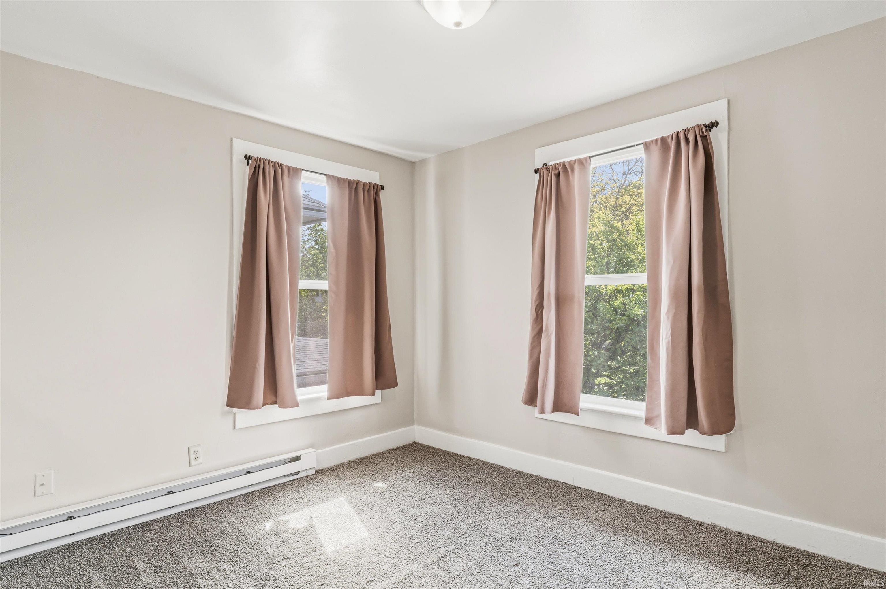 Room featuring two windows with white trim, light neutral wall color, gray carpet, white baseboard, and a ceiling light fixture