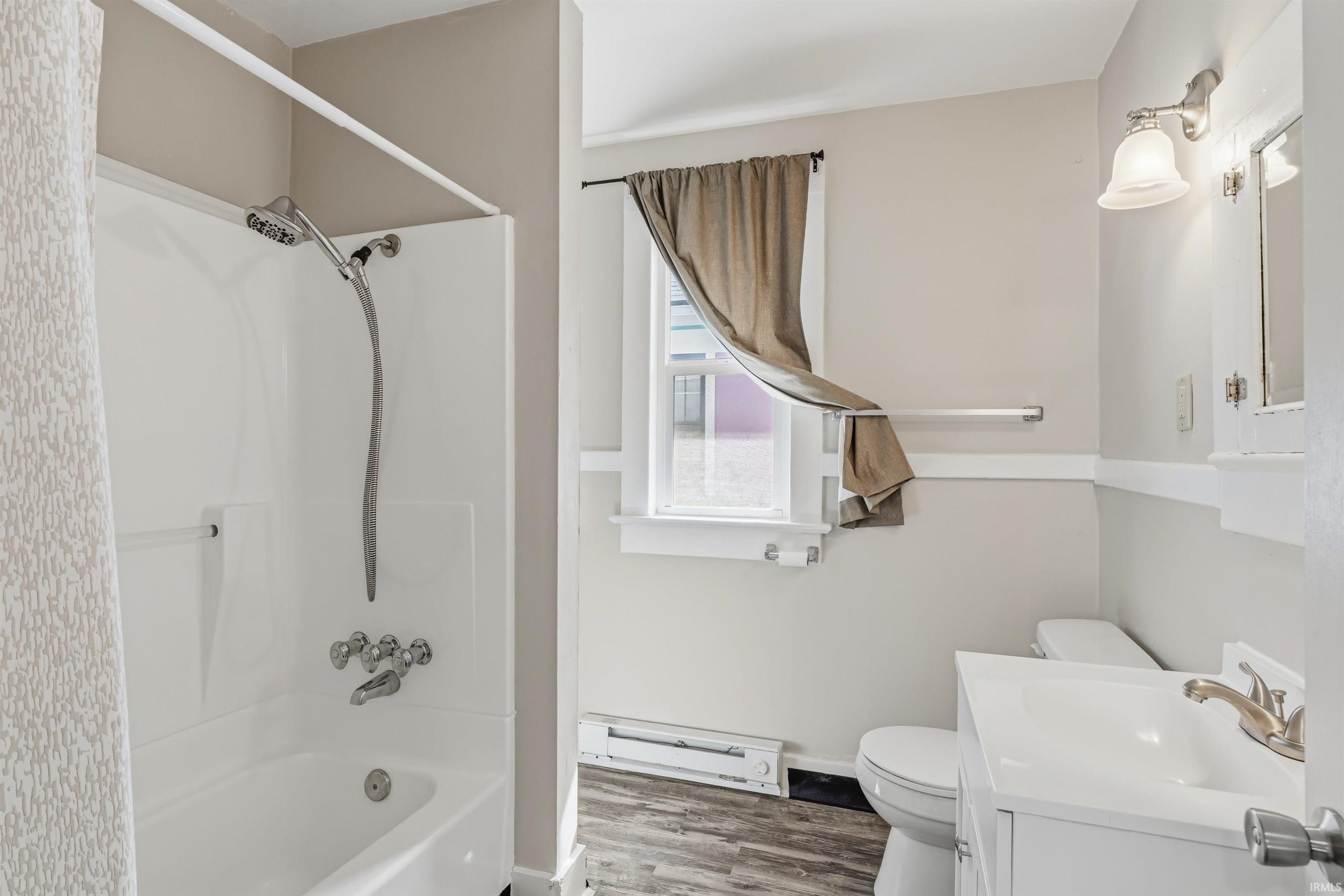 Full bathroom featuring a white tub/shower combination with chrome fixtures, a single vanity with an integrated sink, a built-in medicine cabinet, and wood-finish flooring