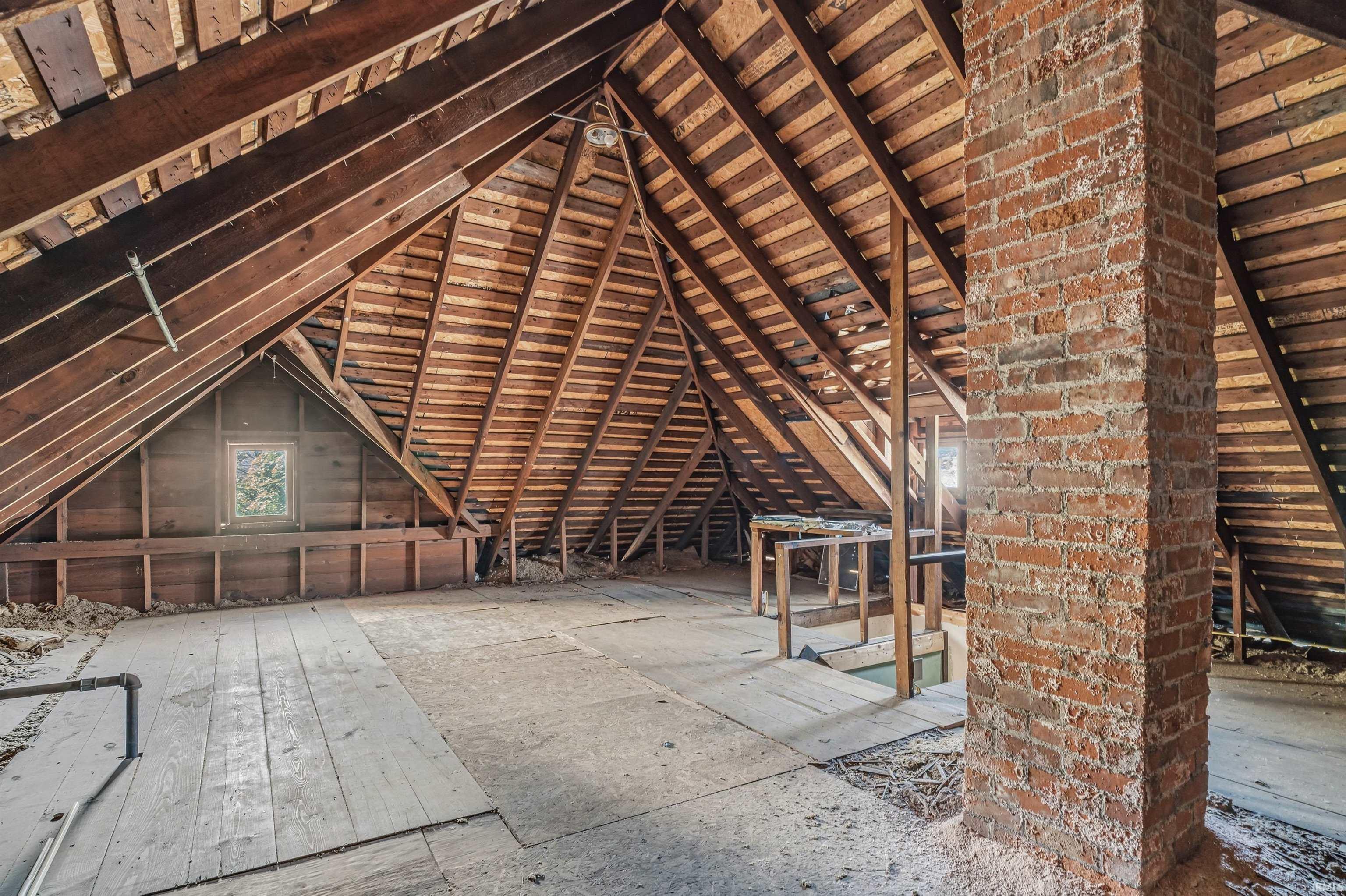 Spacious attic with exposed wood framing, brick chimney, and visible window