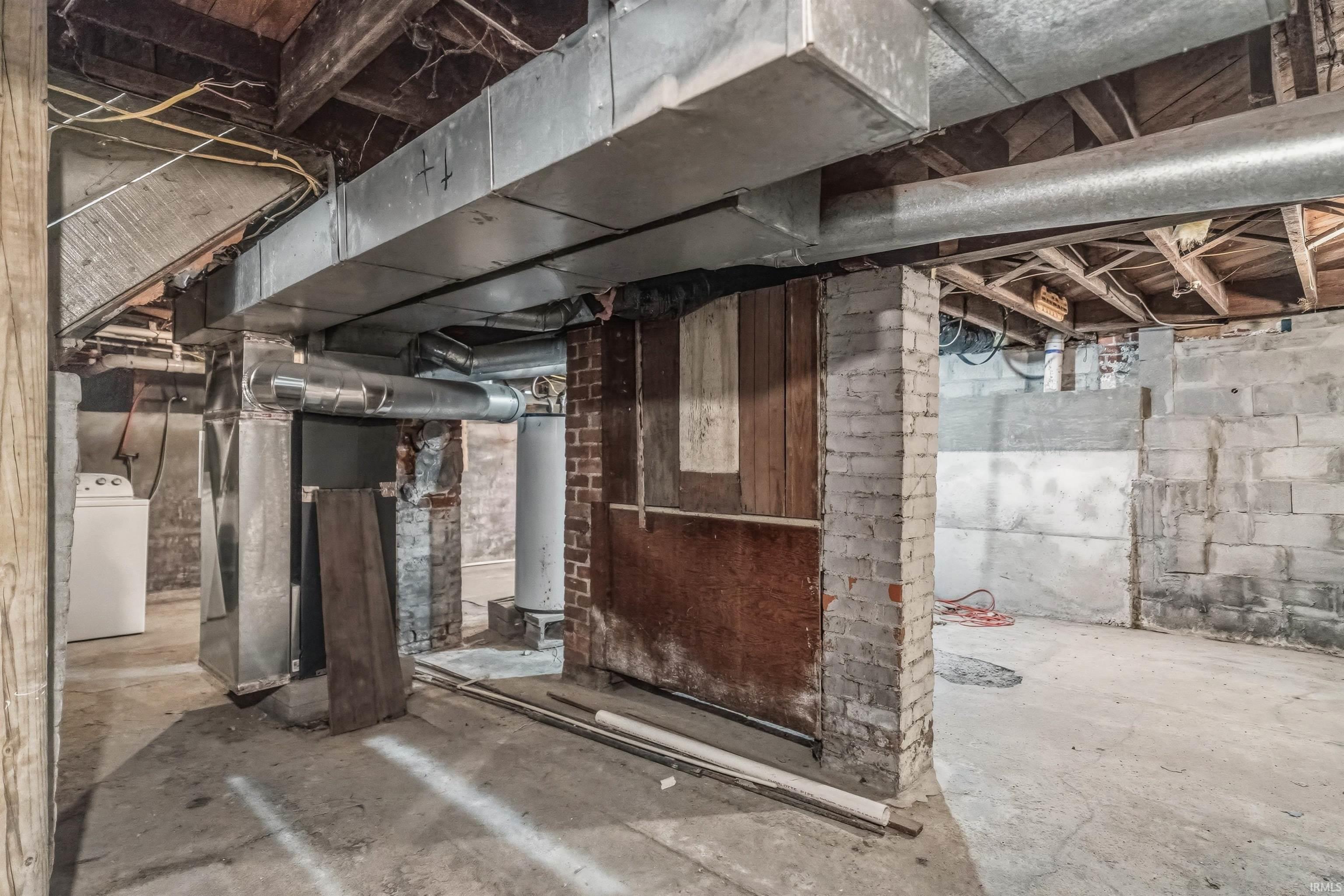 Concrete slab flooring throughout a large unfinished basement with exposed brick support columns and wood beam ceiling
