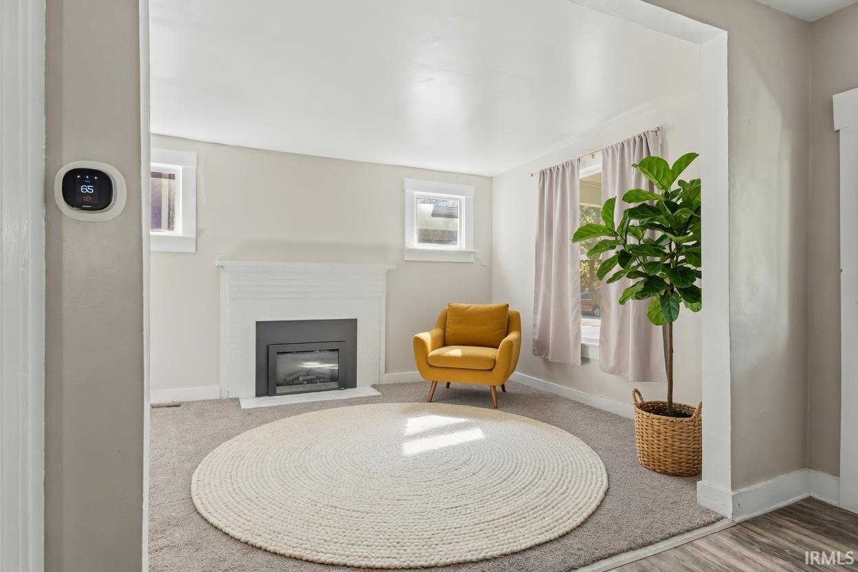 Living area featuring a fireplace with a white mantel, gray carpeting, and multiple windows