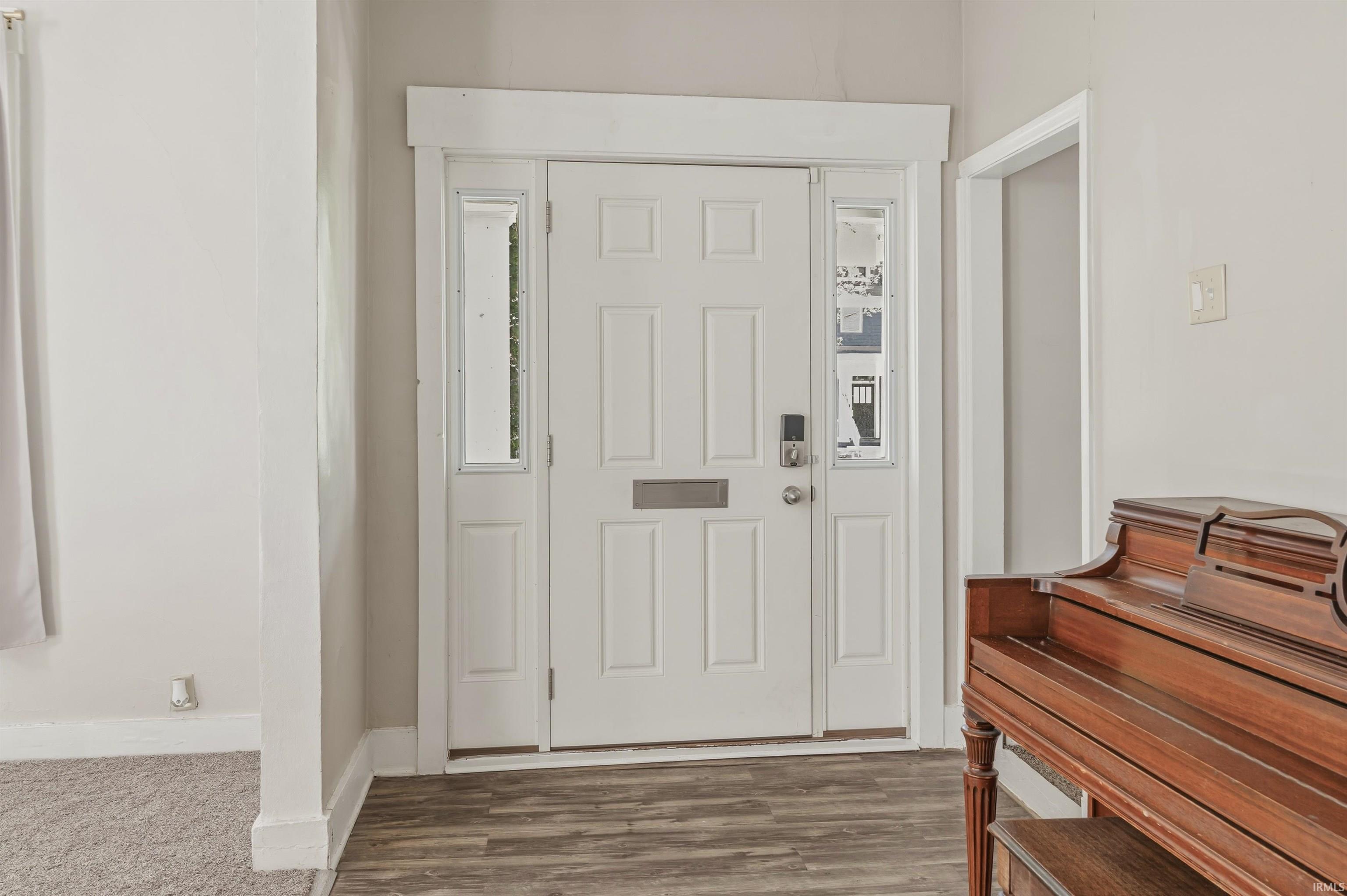Entryway featuring a paneled white front door with sidelights, a transom window, and wood-finish flooring