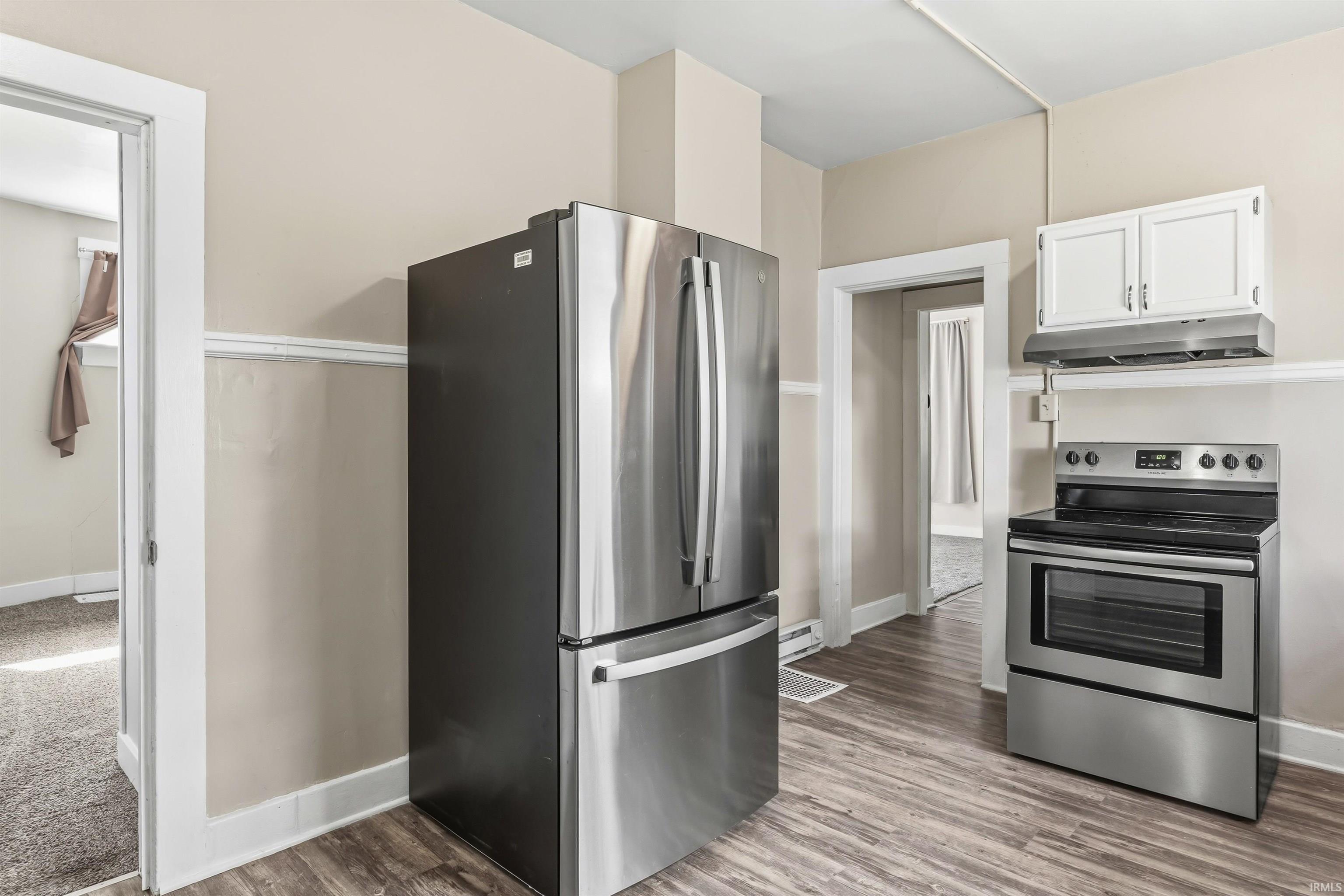 Kitchen featuring wood-finish flooring, stainless steel refrigerator, and stainless steel electric range with overhead cabinetry and range hood