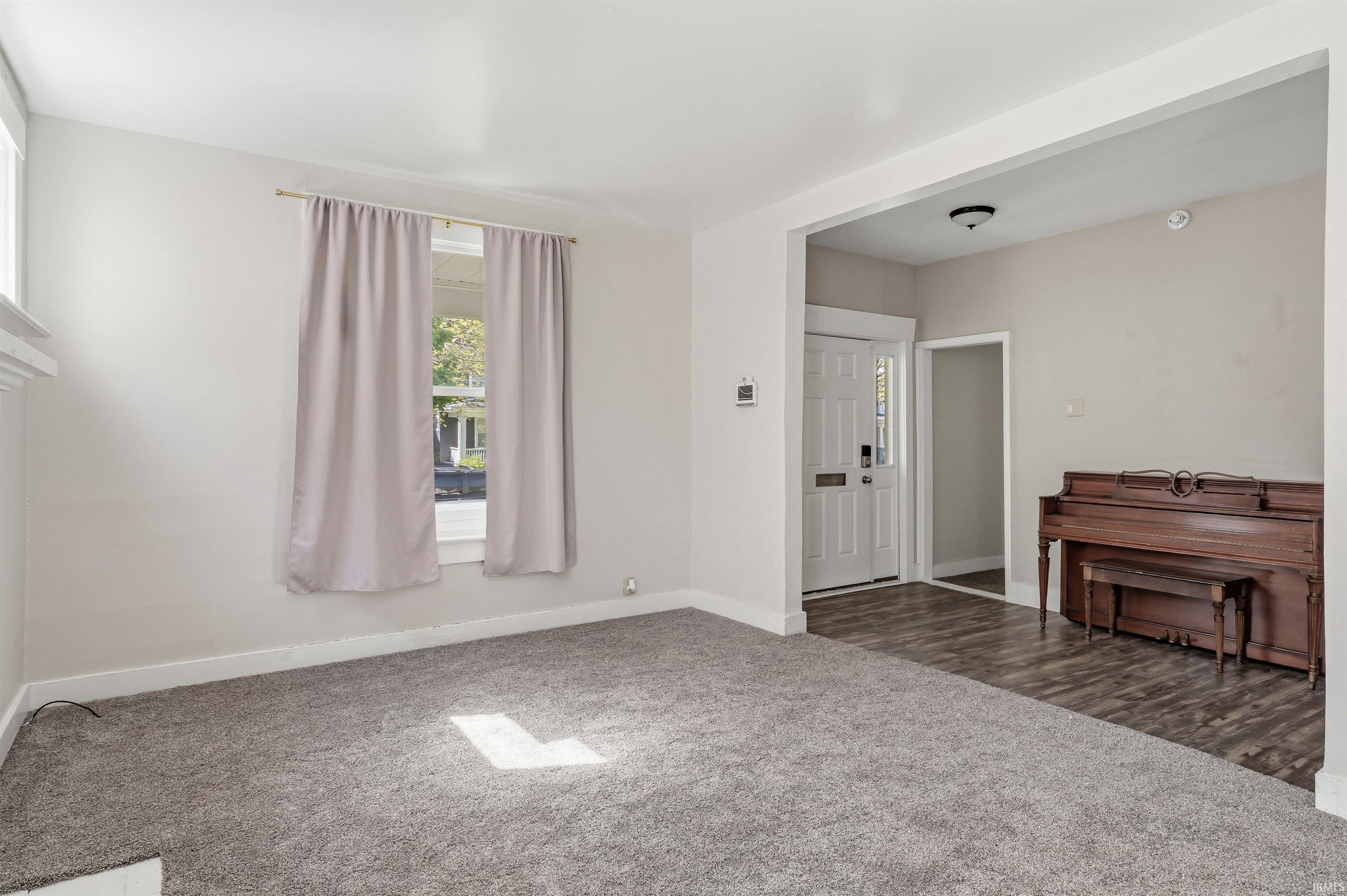 Spacious living area featuring neutral carpeting, white walls, and bright window openings