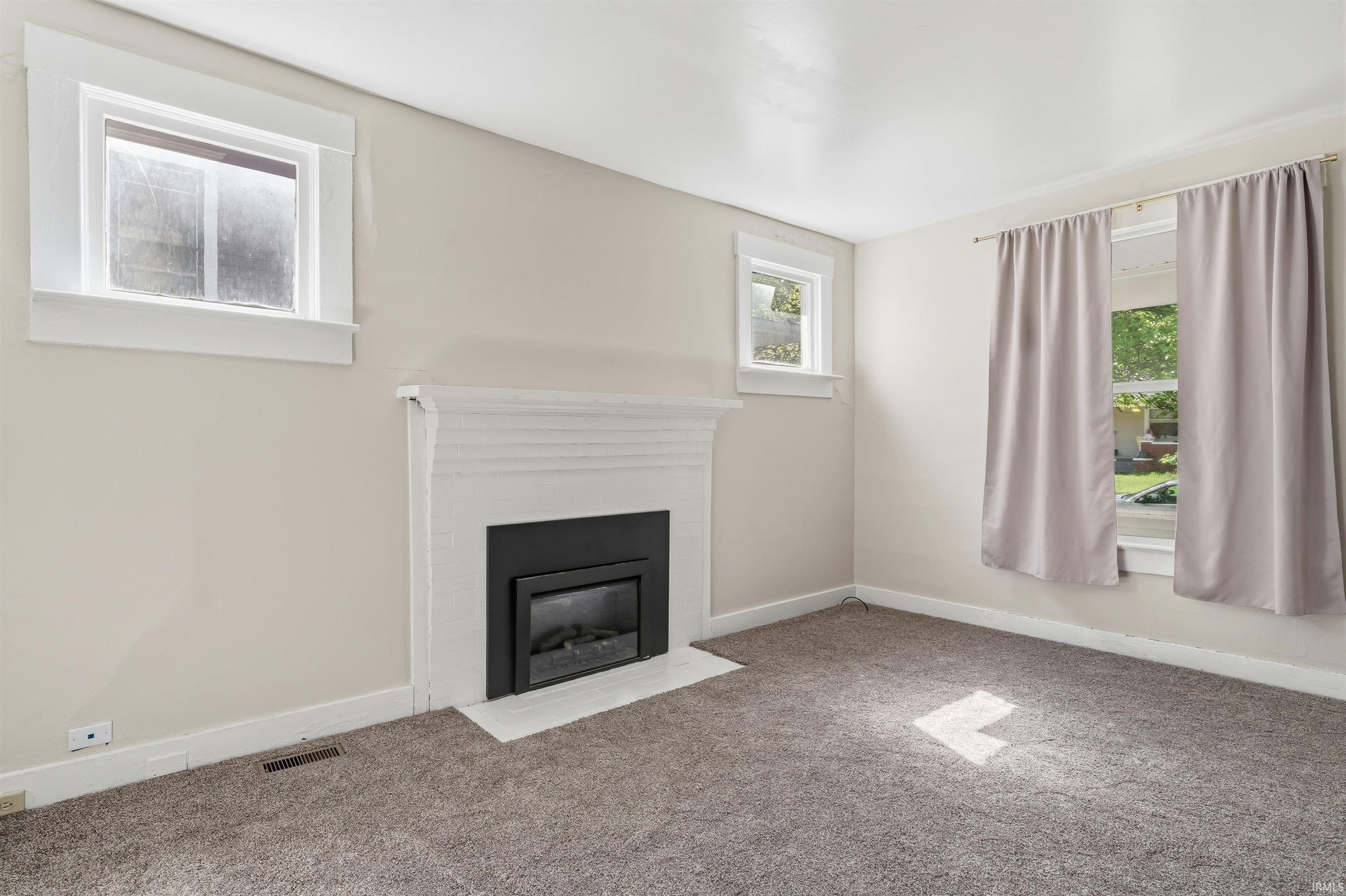 Living space featuring a white mantel fireplace with a black insert, light-colored walls, carpet flooring, and multiple windows with white trim