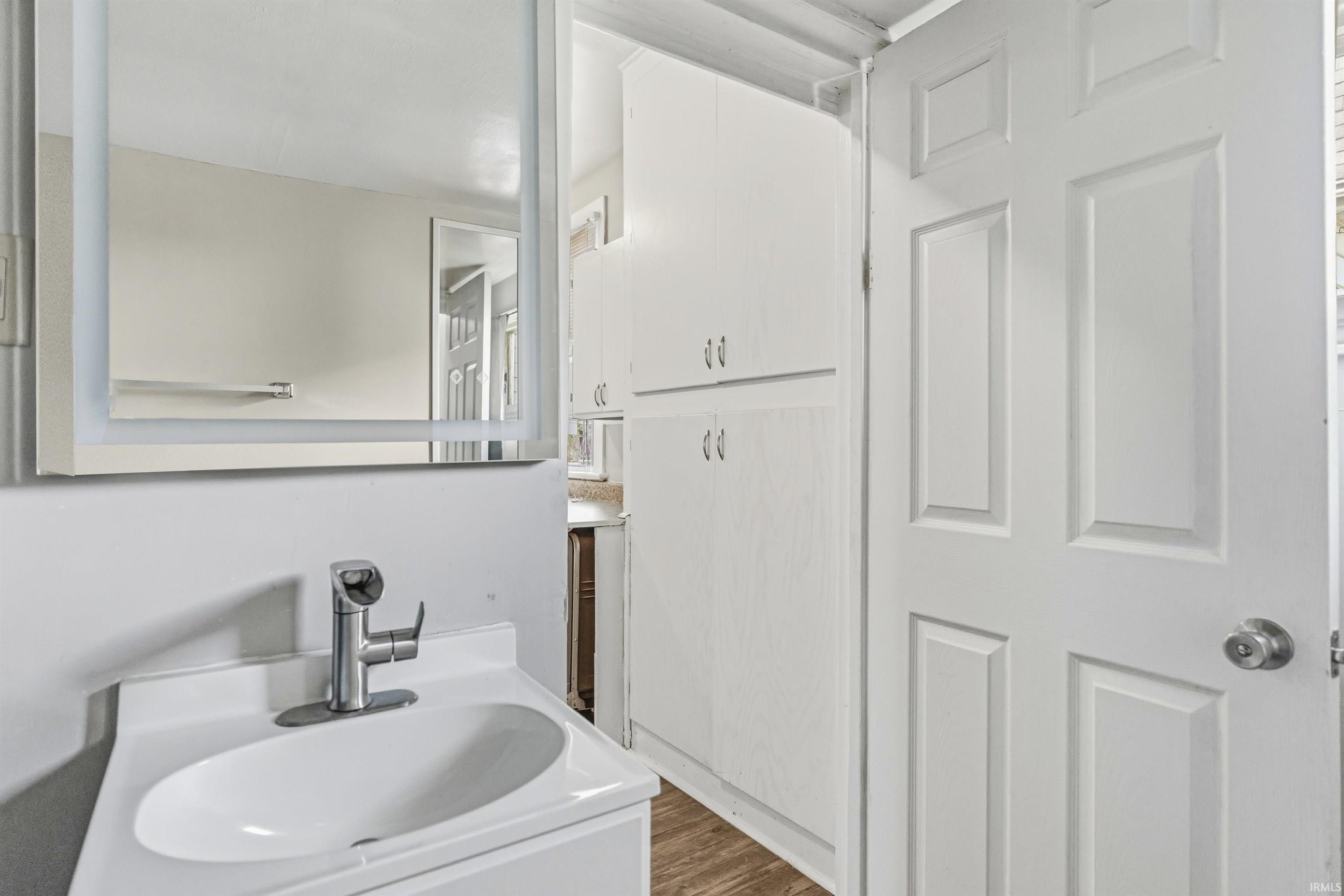 Bathroom featuring a vanity with an integrated sink, brushed nickel faucet, an illuminated medicine cabinet, extensive built-in storage cabinetry, and wood-finish flooring
