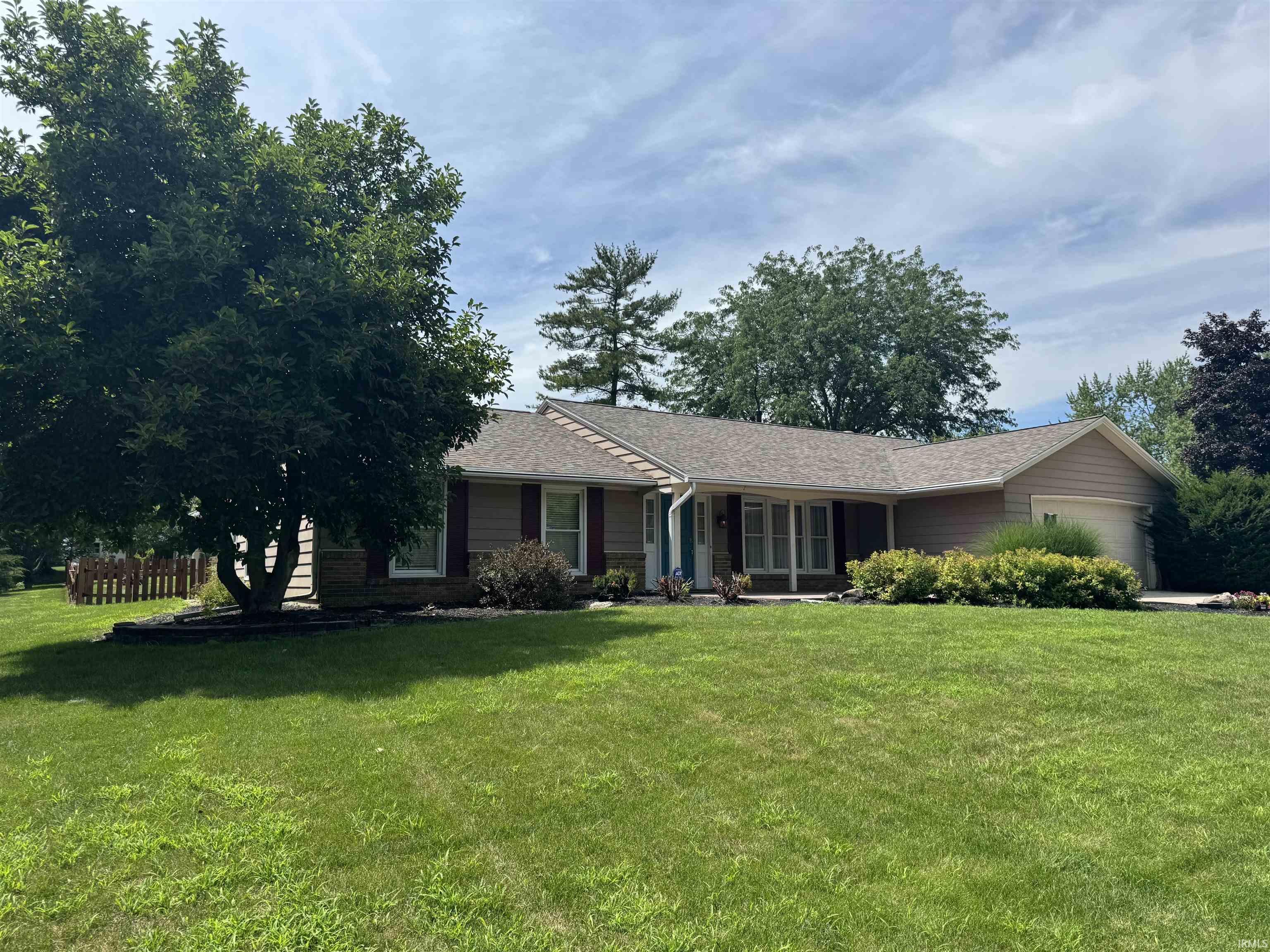 Ranch-style residence featuring a prominent front lawn, mature shade trees, and a two-car garage