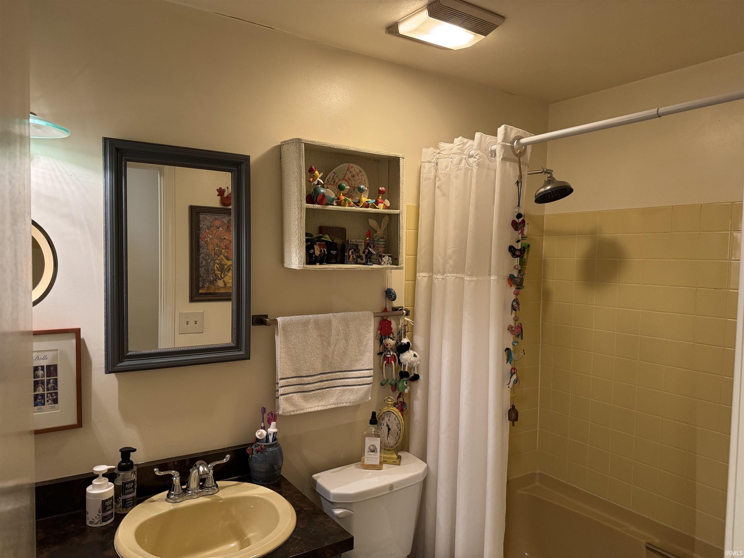 Bathroom featuring a built-in shower/tub combination with ceramic tile surround, a vanity with an integrated sink, a framed wall mirror, a wall-mounted towel bar, and a built-in wall shelf
