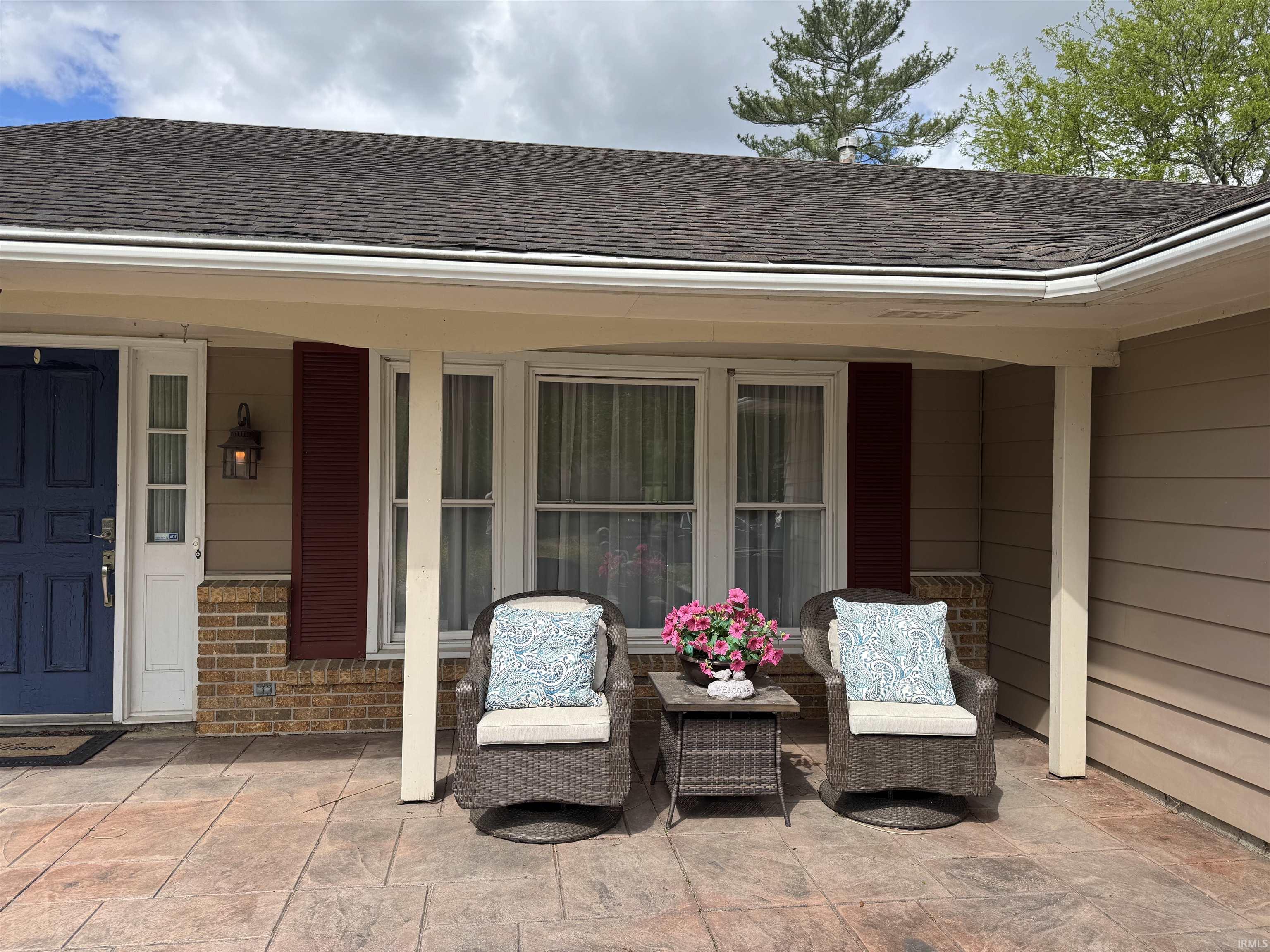 Covered front patio featuring stamped concrete, a prominent blue entry door, brick accents, and a classic outdoor wall lantern