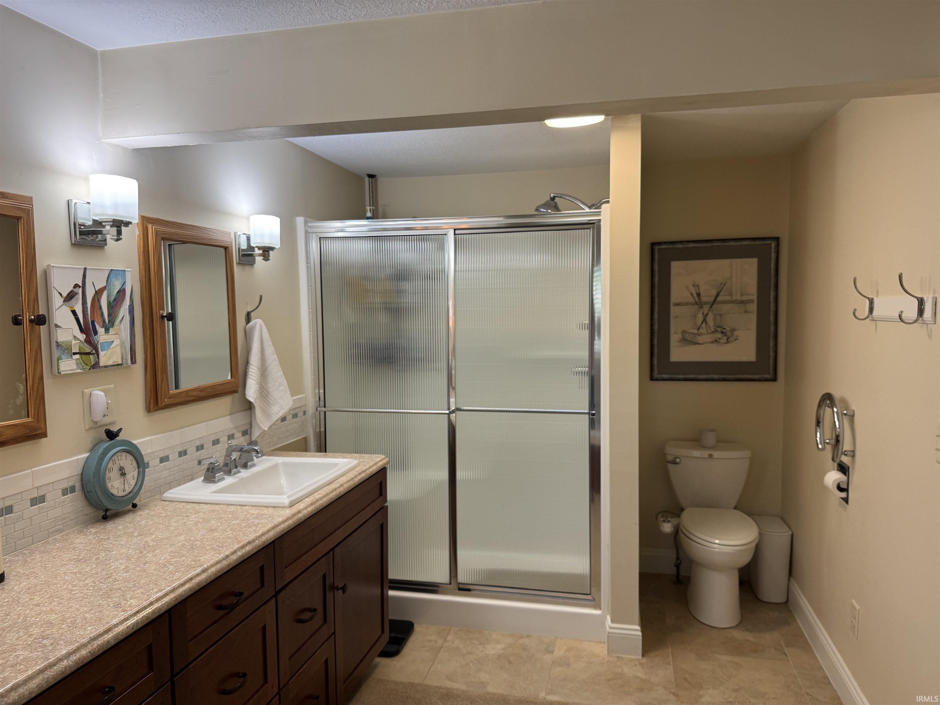 Bathroom featuring a dark wood vanity with a single integrated sink, speckled countertop, and mosaic tile backsplash