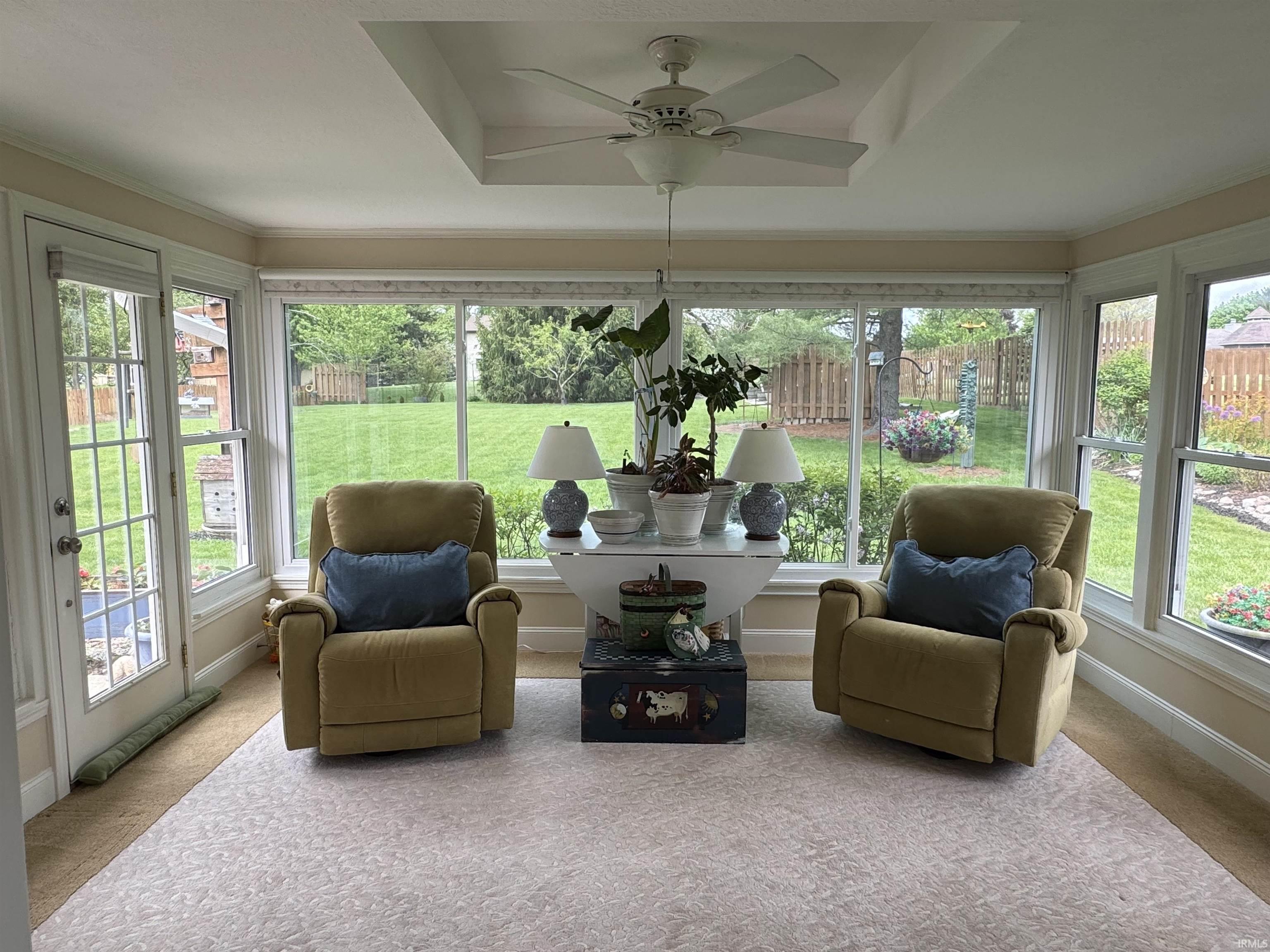 Sunroom featuring extensive window-lined walls, a tray ceiling with a built-in ceiling fan, and carpeted flooring