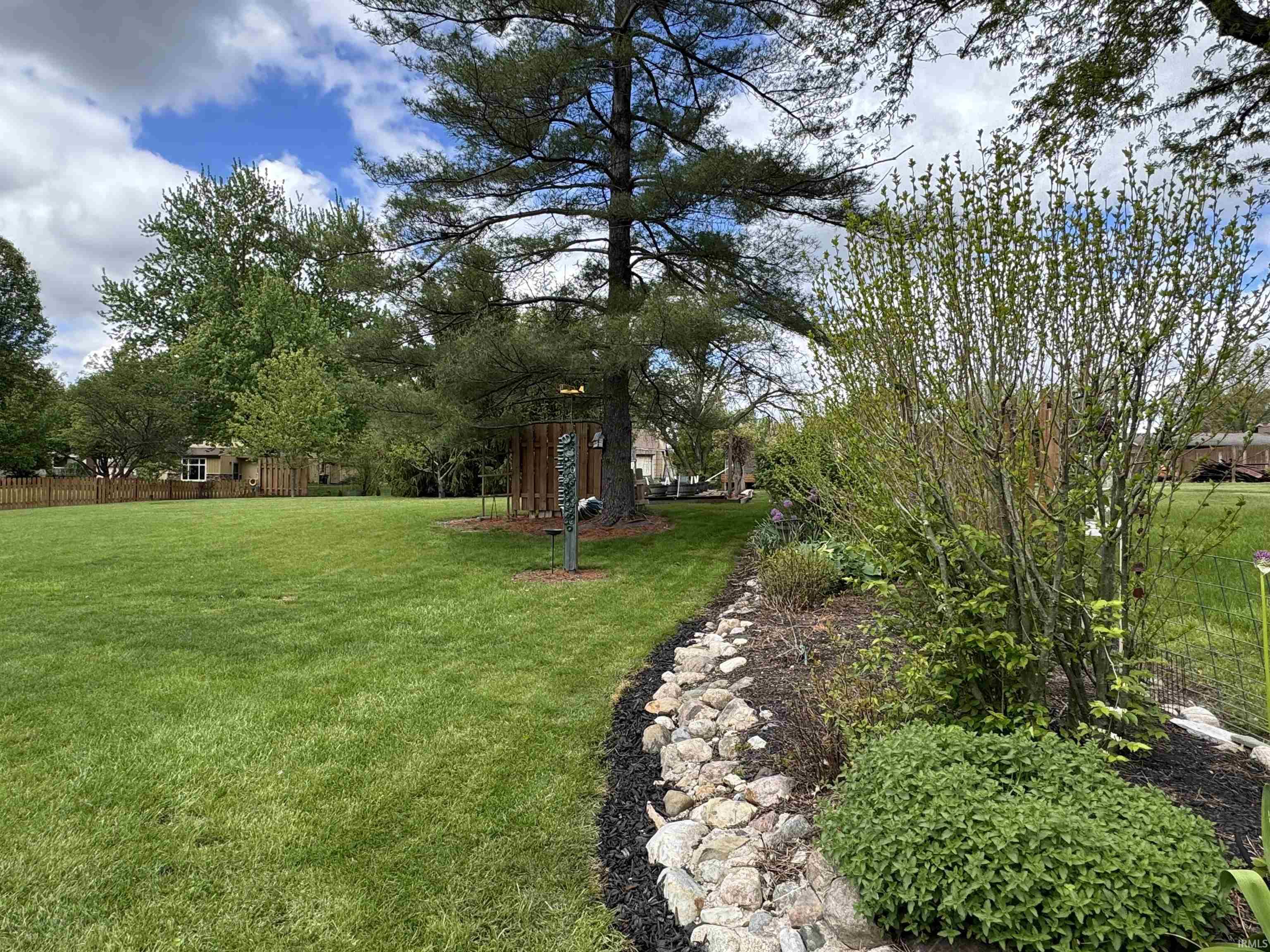 Expansive green lawn featuring mature trees and a decorative rock-lined garden bed with assorted plantings
