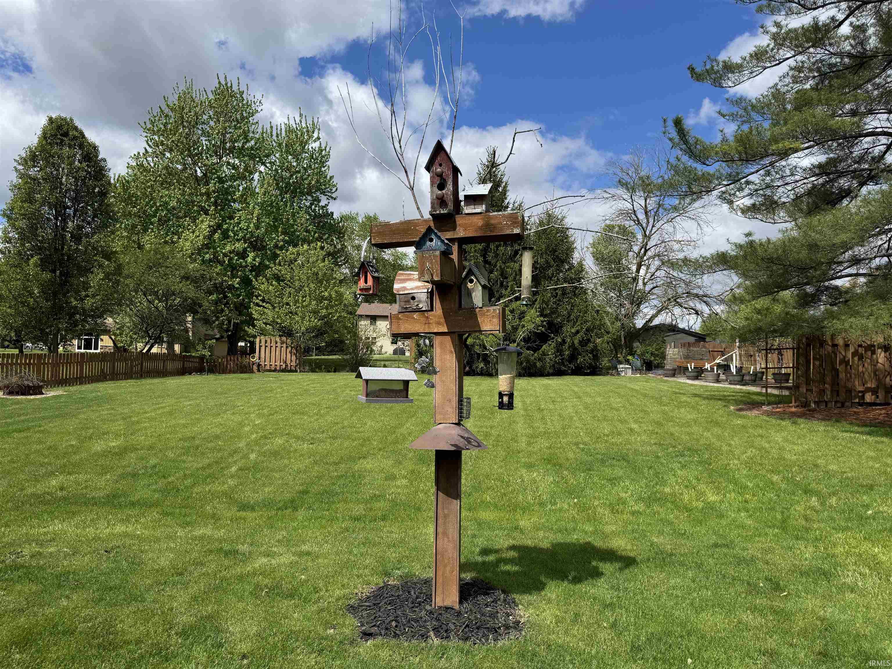Expansive lawn space featuring mature perimeter trees, a decorative birdhouse post, and partial fencing
